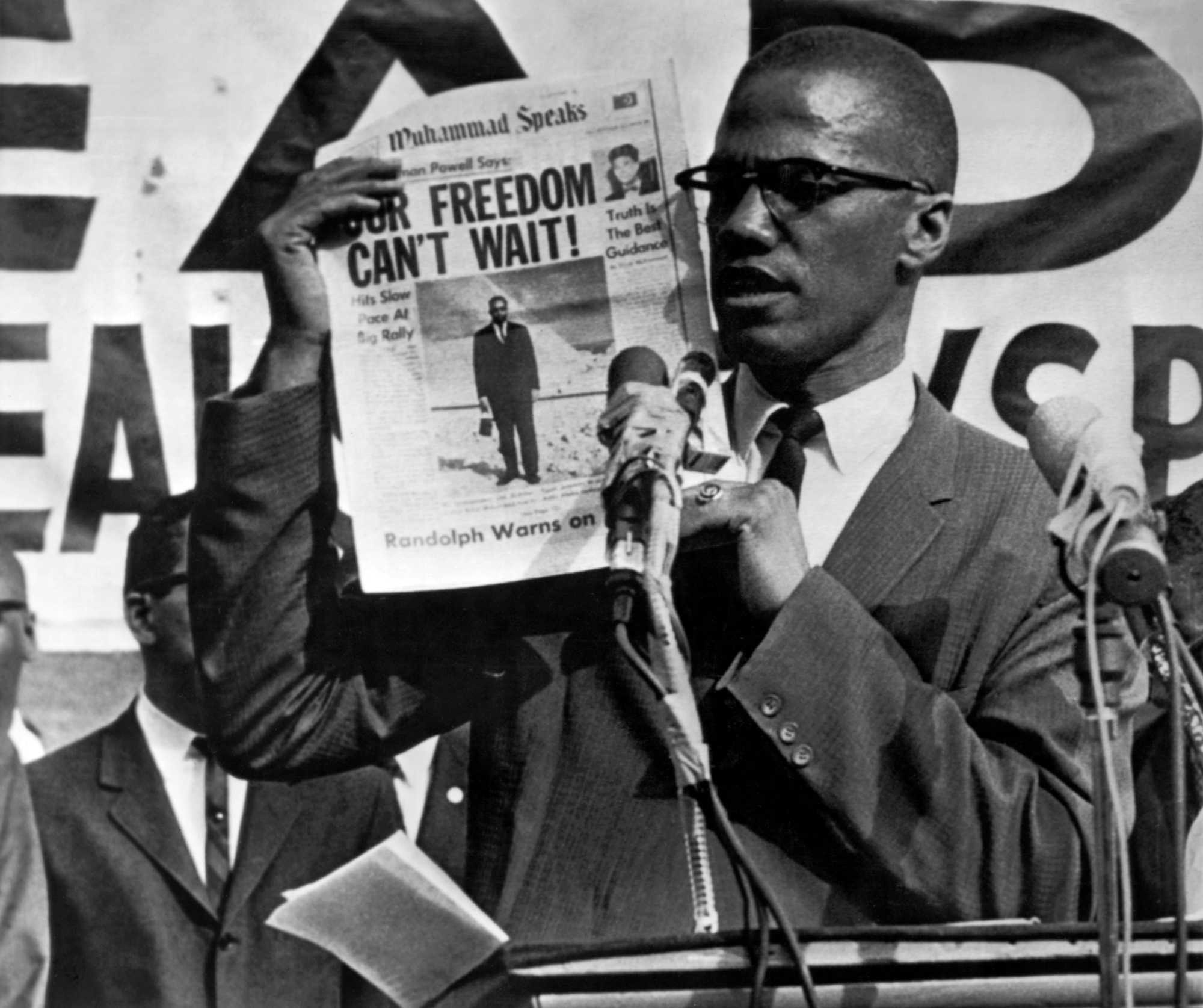 Malcolm X holds up an issue of Muhammad Speaks newspaper during a rally in Harlem, New York City