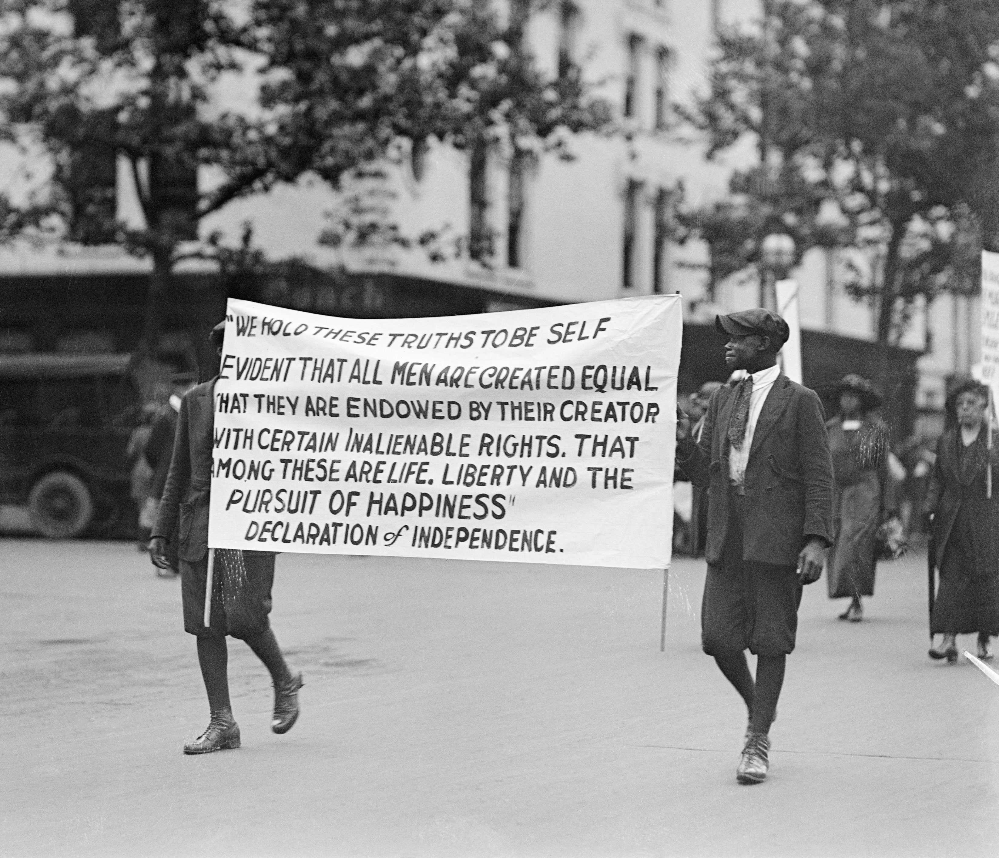 A black and white of two young black protesters holding a large banner quoting the Declaration of Independence.