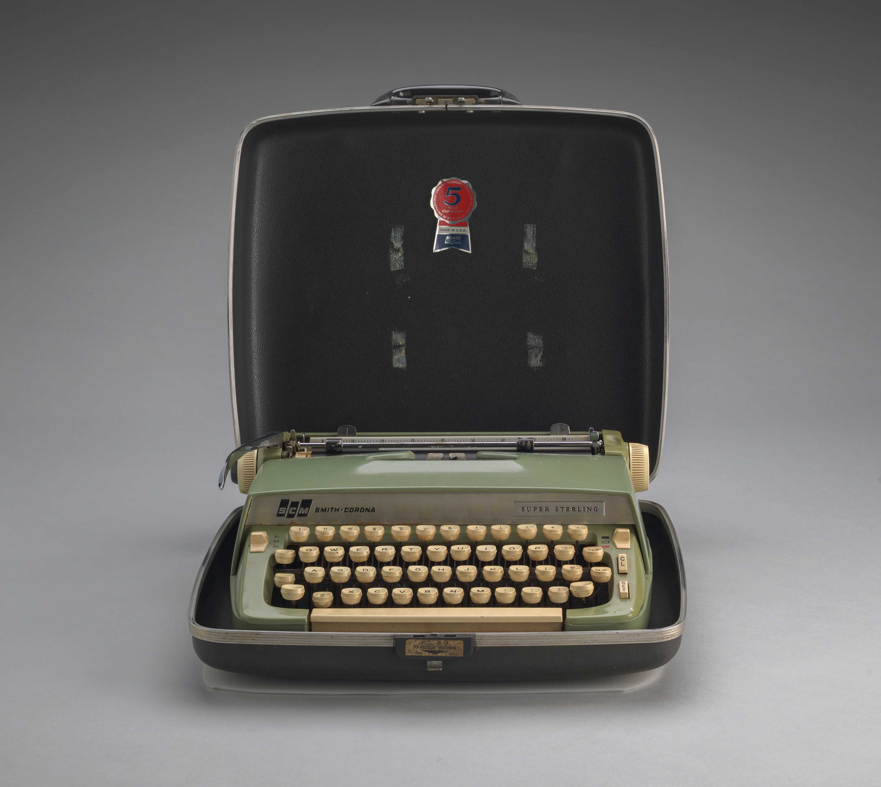 A light green typewriter with beige keys sitting inside an dark gray open case.