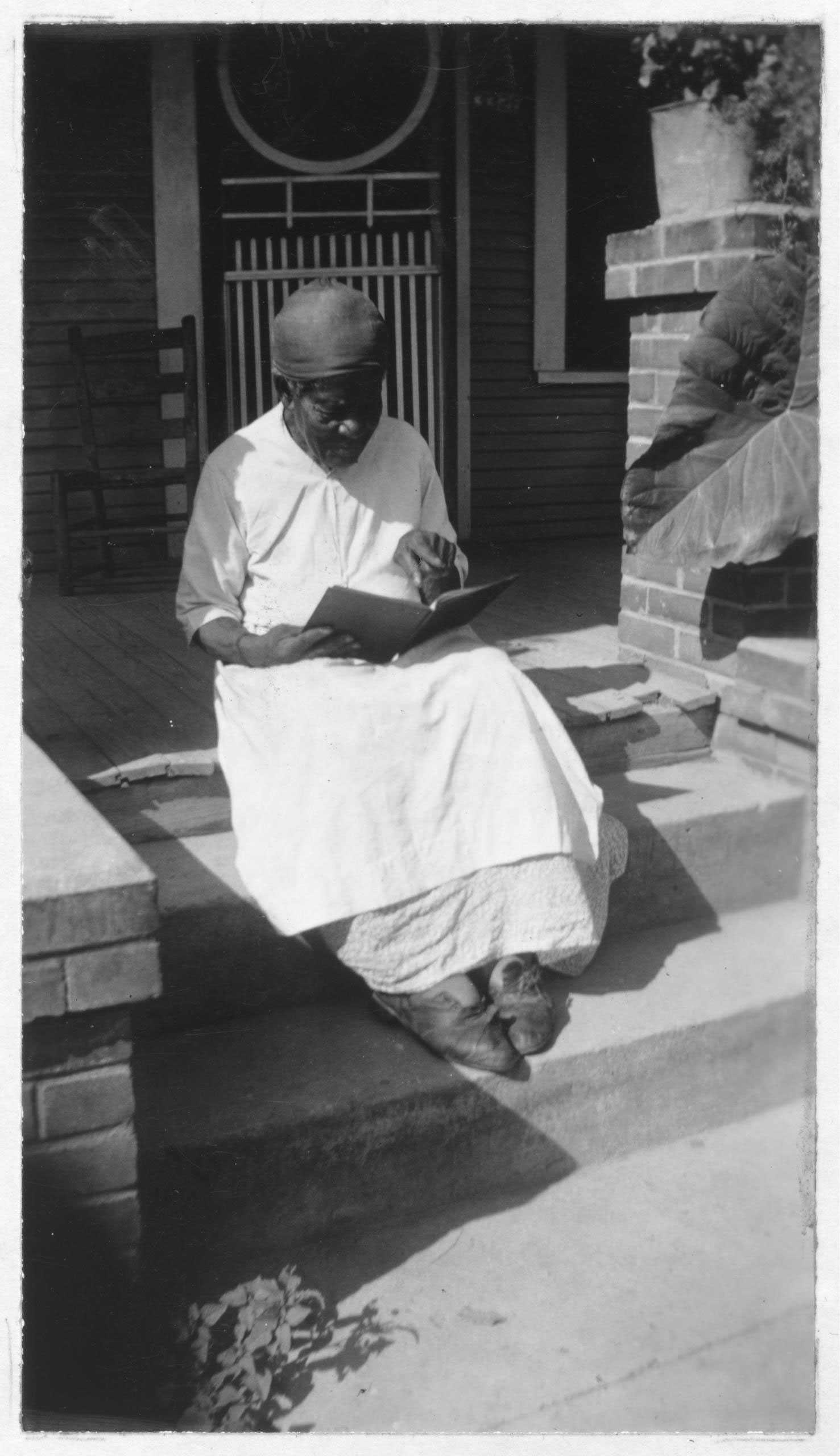 A black and white photograph of Mary Armstrong is reading a book on a front step of a house.