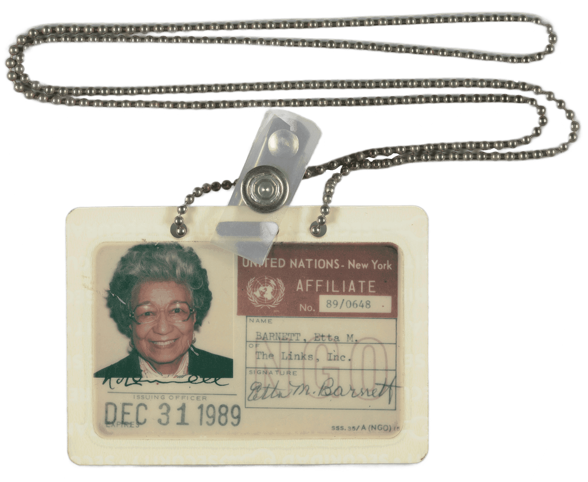 United Nations ID card belonging to Etta Moten Barnett. It is a plastic laminated card with a color photograph of Etta Moten Barnett in the top left hand corner. In the photograph Etta Moten Barnett is depicted from the shoulders up. She is wearing a black top, a pink scarf around her neck and glasses.