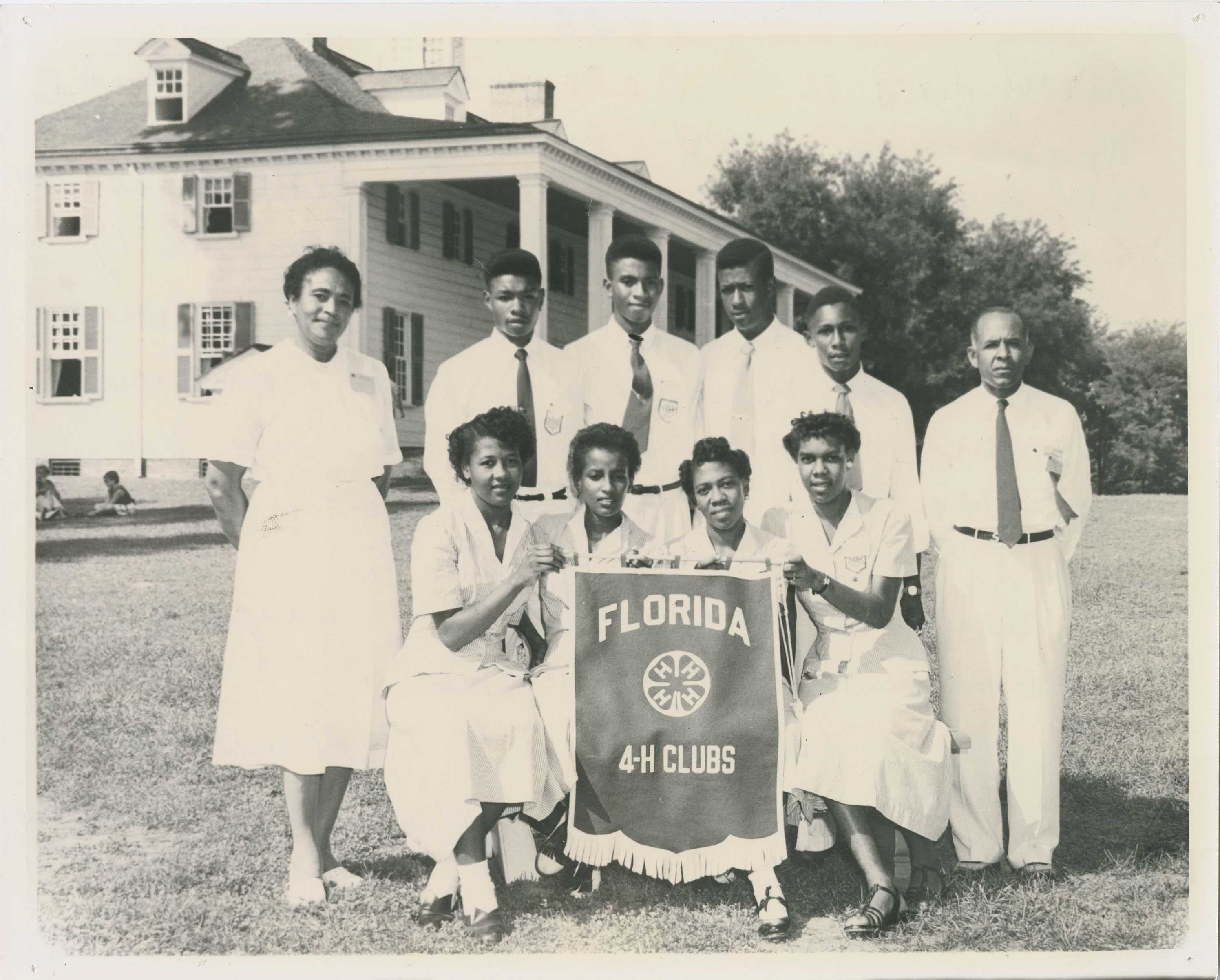 A group photo of men and women holding a Florida 4-H Clubs banner, standing in front of a large building.