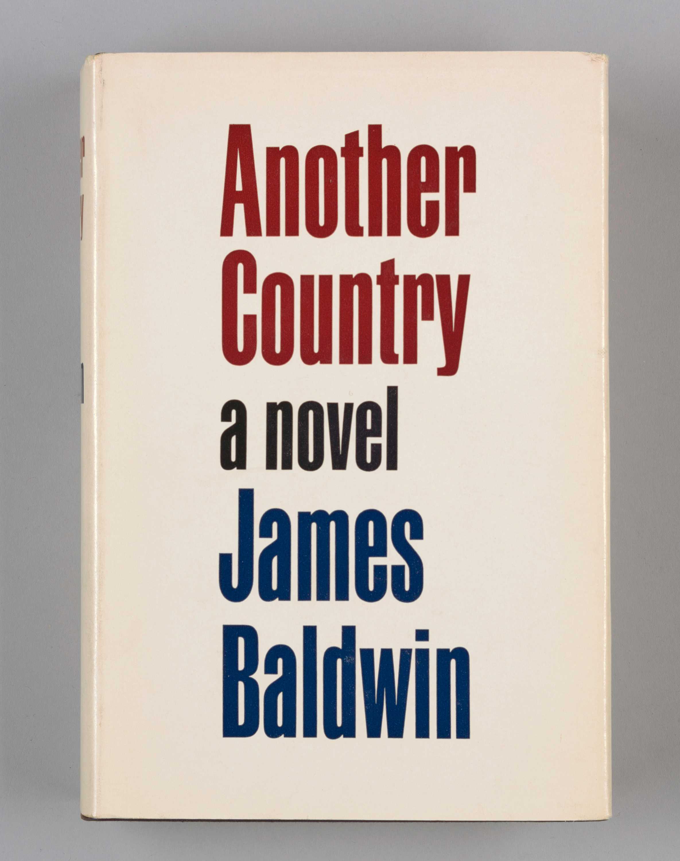 A hardback book titled Another Country by James Baldwin. The exterior has a paper book cover and a clear plastic book cover over that. The paper book cover is off-white with red text, centered, that reads: [Another / Country] and dark blue type, centered, that reads: [a novel / James / Baldwin] in large font on the front cover. The binding, in same color scheme, reads: [Another / Country / James / Baldwin / Dial]. The back cover of the paper sleeve, bordered by solid red line, has text in black and red type that gives a bulleted-list synopsis of eight characters in the book. The front interior of paper sleeve gives a synopsis of the book, while the back interior of the paper sleeve has a black-and-white depiction of James Baldwin and gives information, in black type, about his life and career. Hardback cover itself is black with white type and red on interior front and back covers. On the inside cover there is a white sticker that in black print reads: [From the Library of Albert Tsugawa]. The interior pages, 436 in total, are off-white paper with black type.