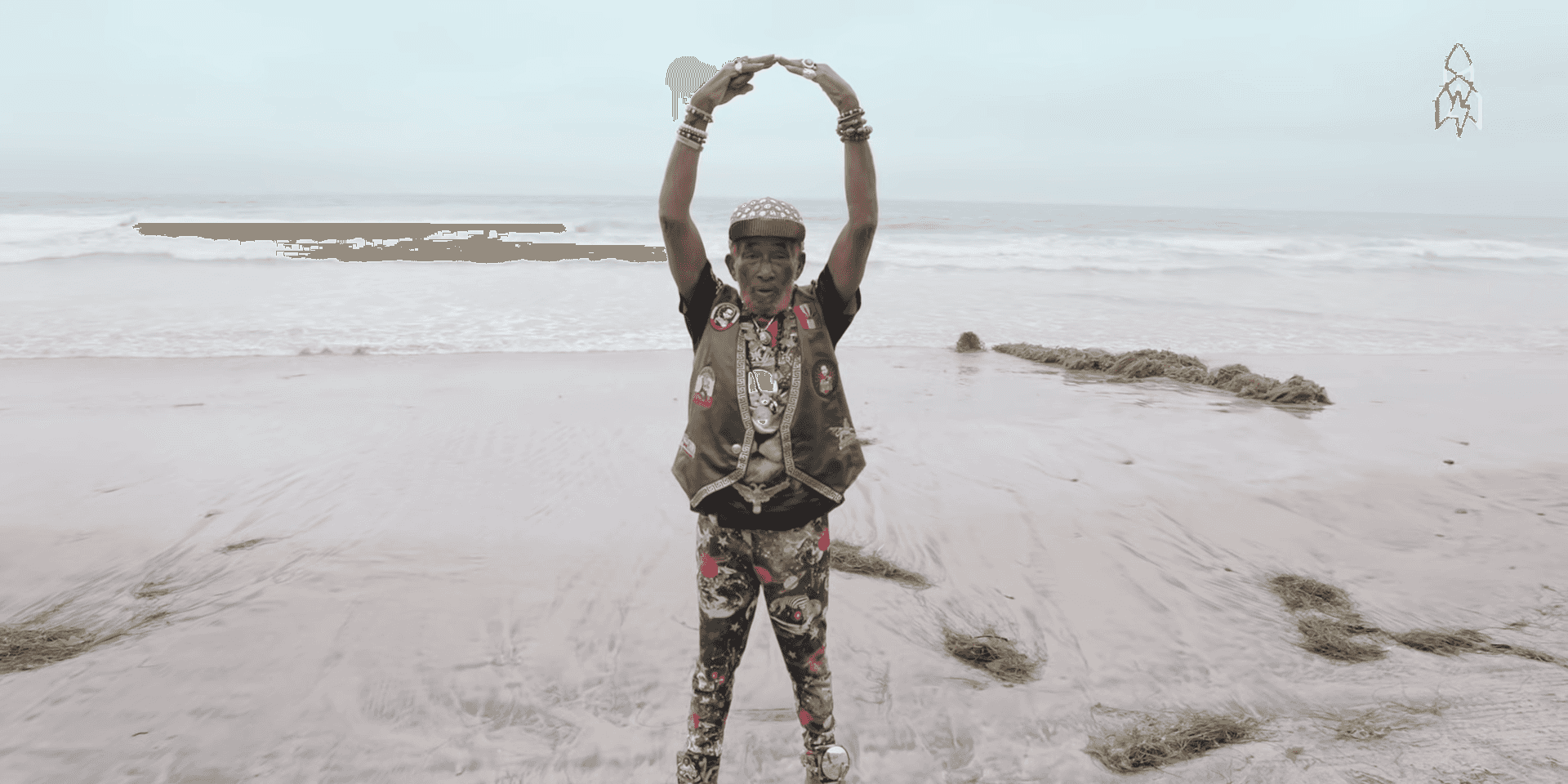 A man is standing on a beach with his hands up in the air to create a large circle.