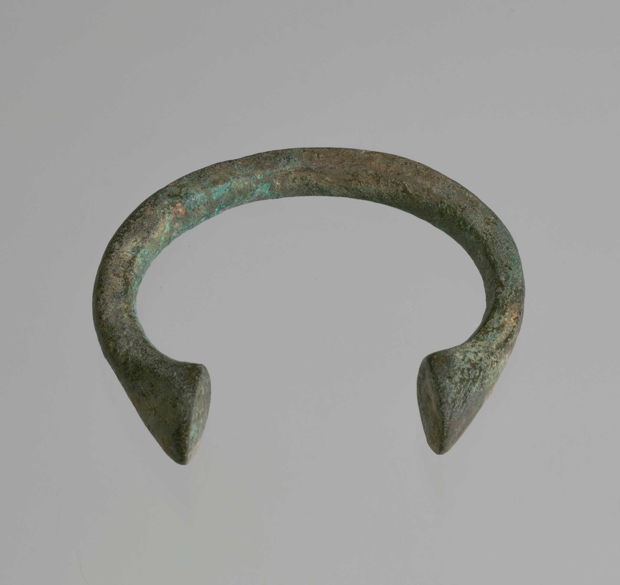 Manilla, a form of currency that circulated in West Africa, in a semi-circular horseshoe shape, with slight flairs at ends.
