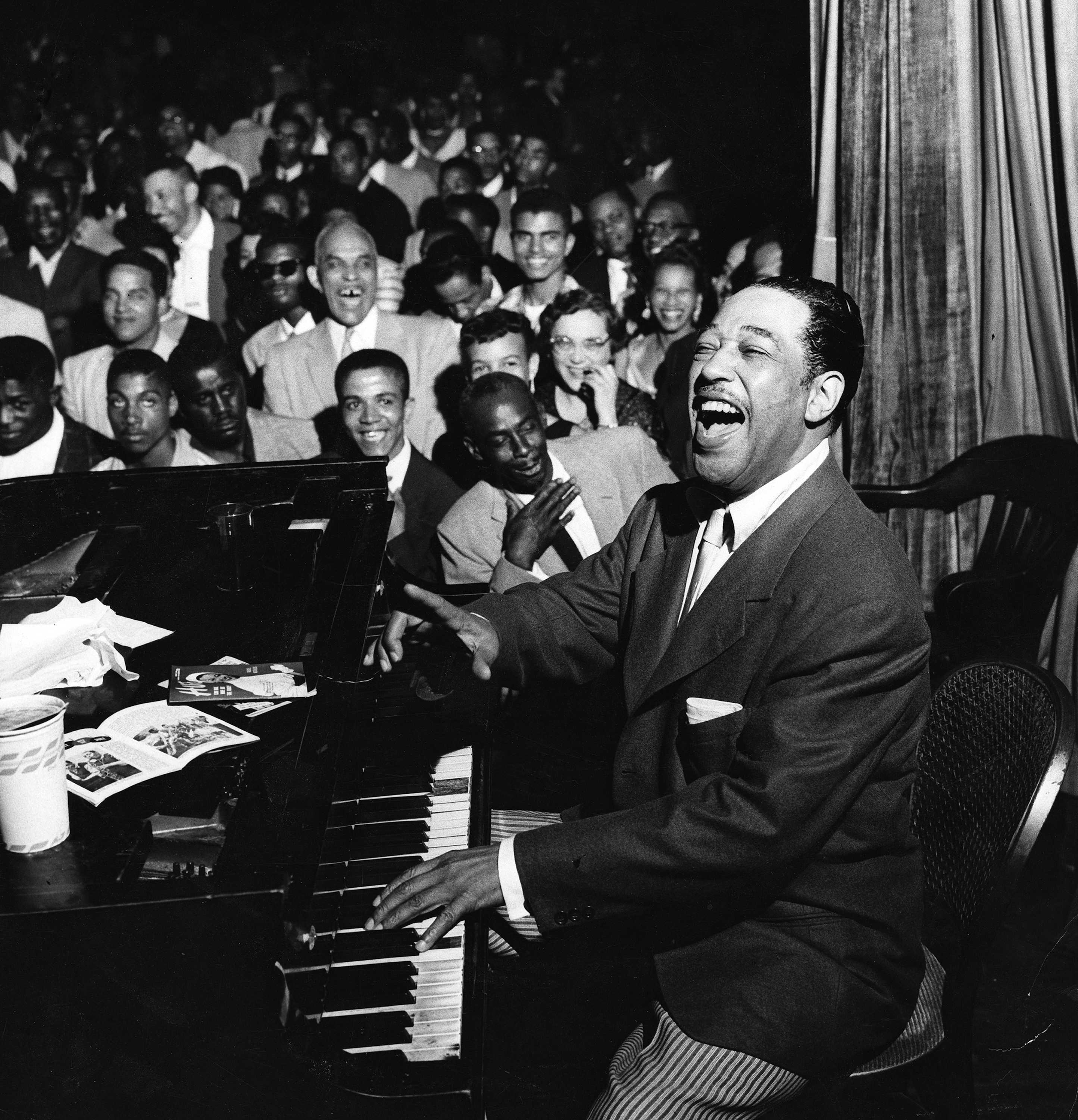 Black and white photograph of Duke Ellington sitting at a piano in front of a crowd