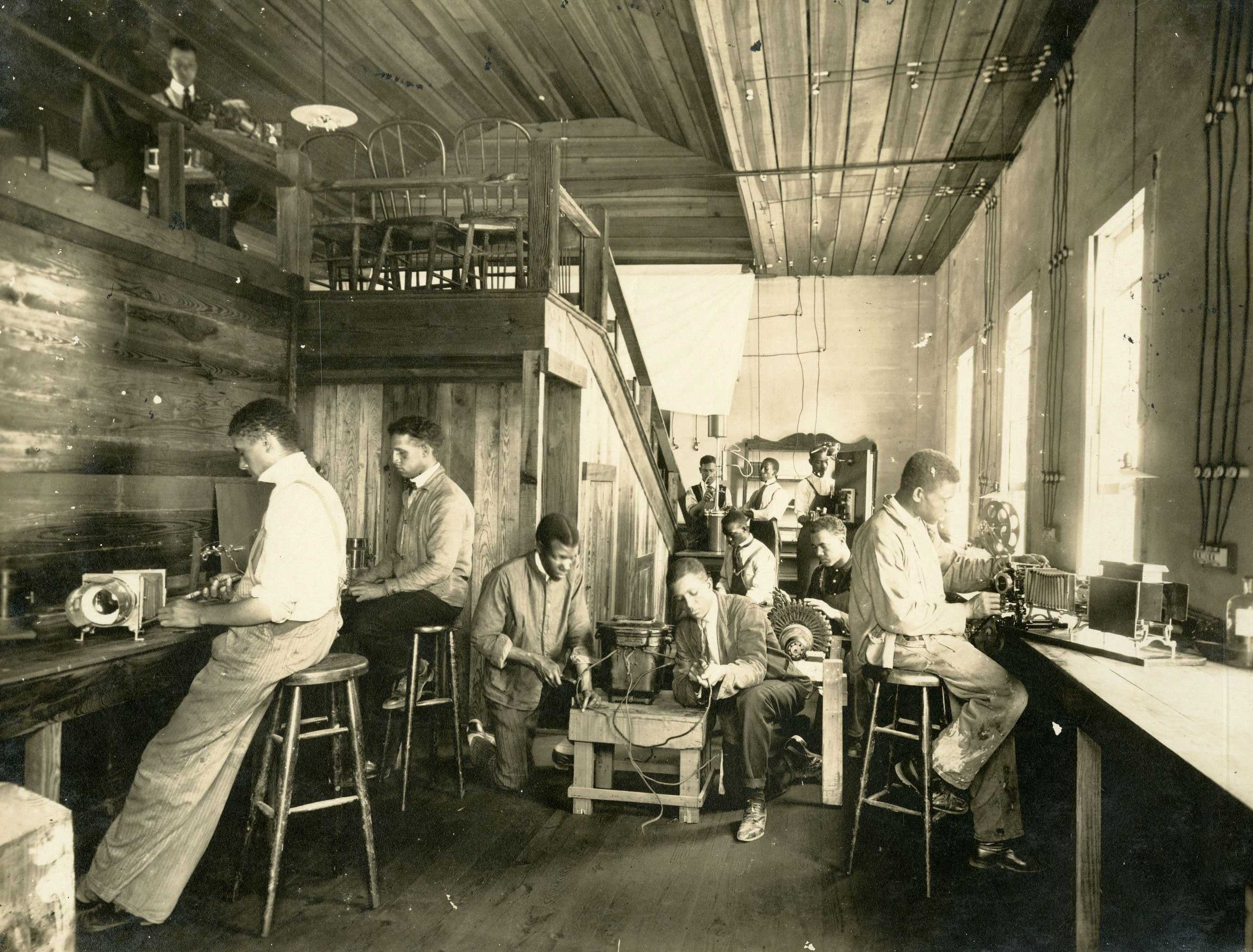 Photo of men working with electrical equipment in a room, illustrating early 20th-century laboratory work.