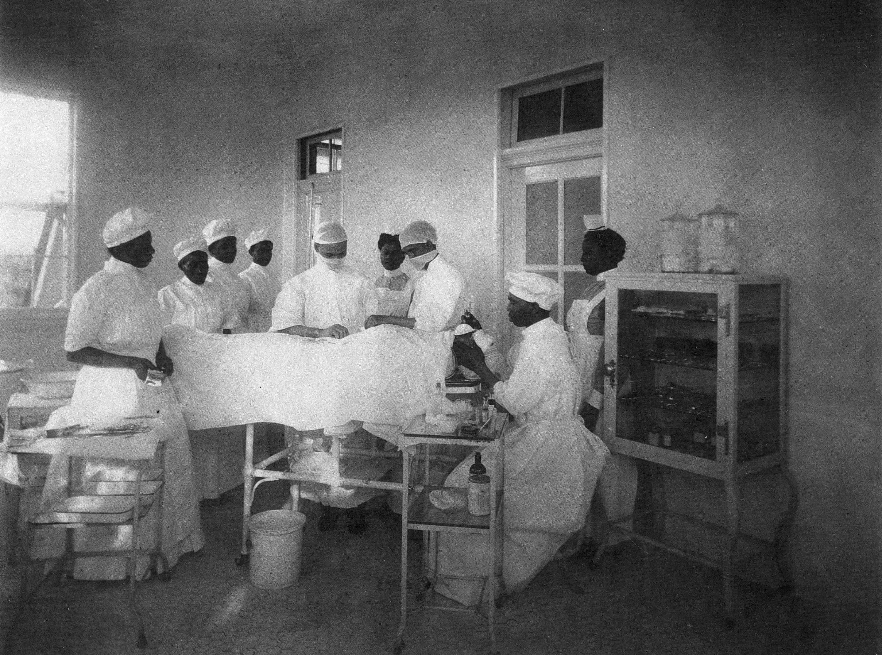 Photo of a surgical operation with doctors and nurses gathered around an operating table in a hospital room.