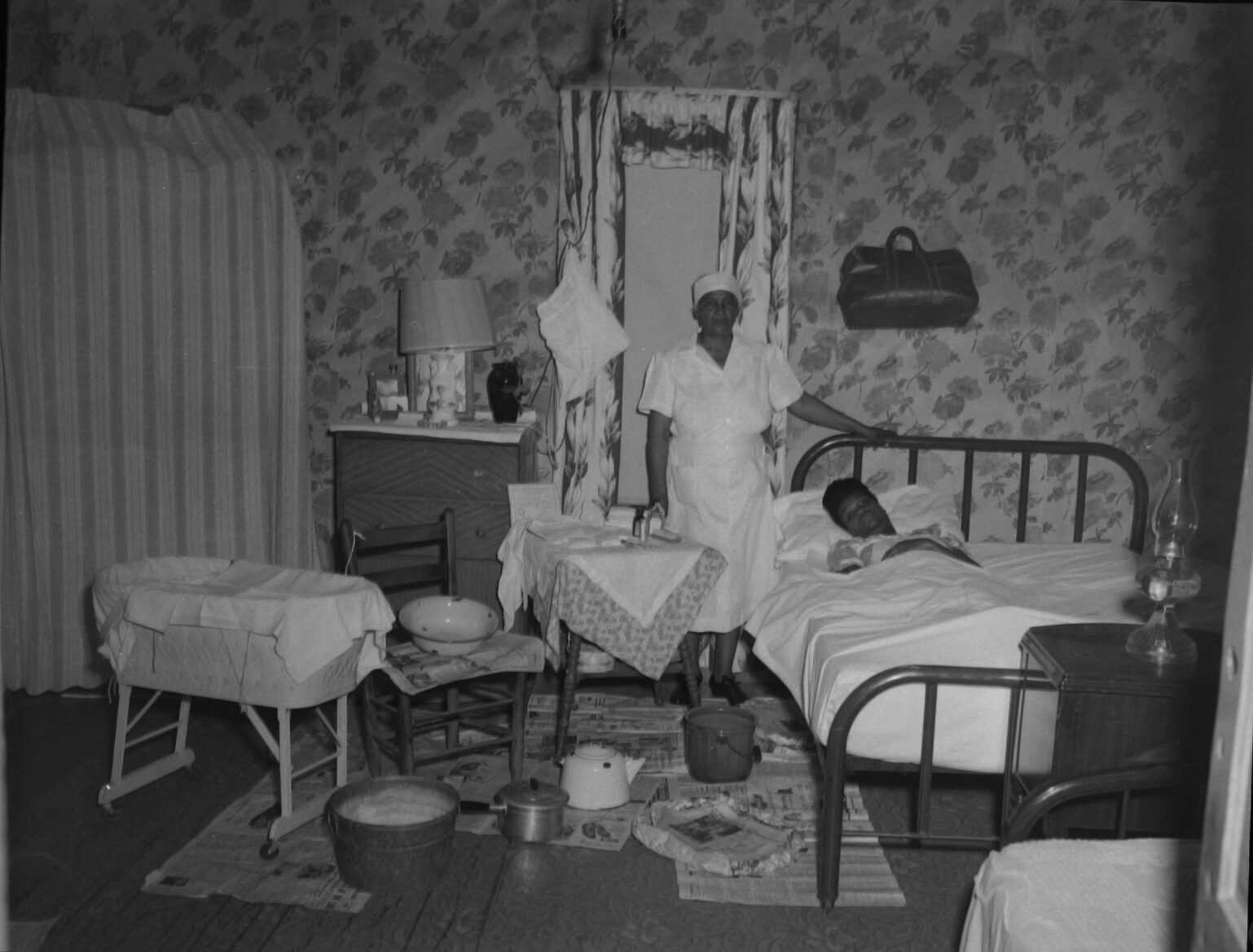 Indoor portrait of a midwife standing next to a woman who is laying down in a bed.