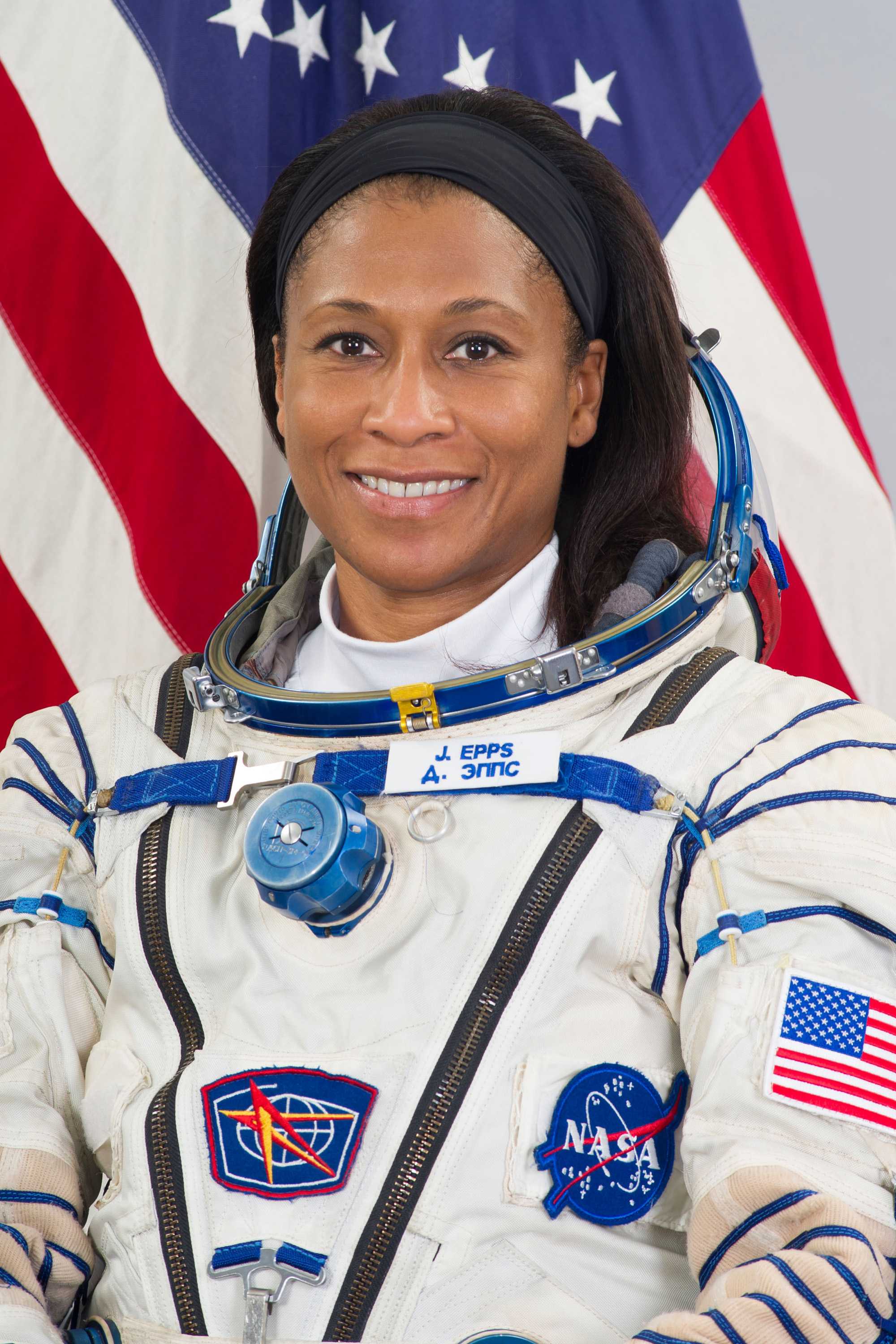 Jeanette Epps is wearing a white space suit with NASA logos and patches while smiling for a portrait.