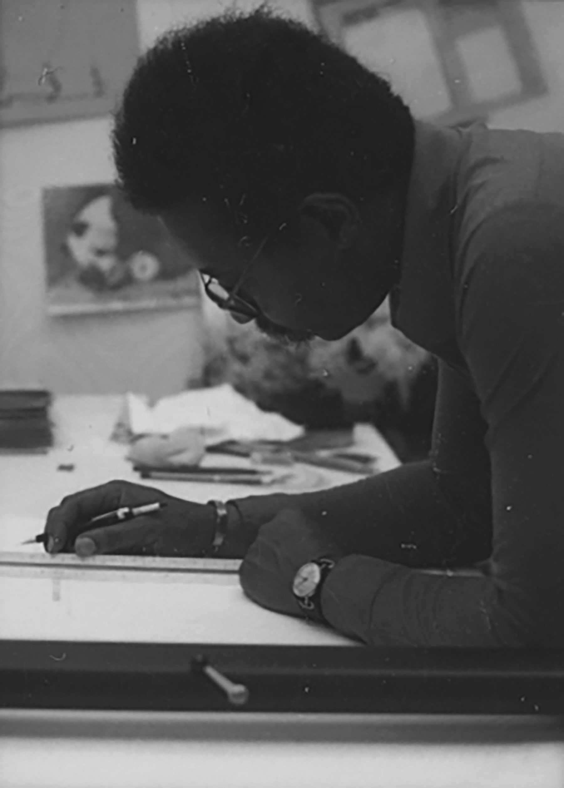 Black-and-white photo of a person using a pen and ruler to work on a drawing.