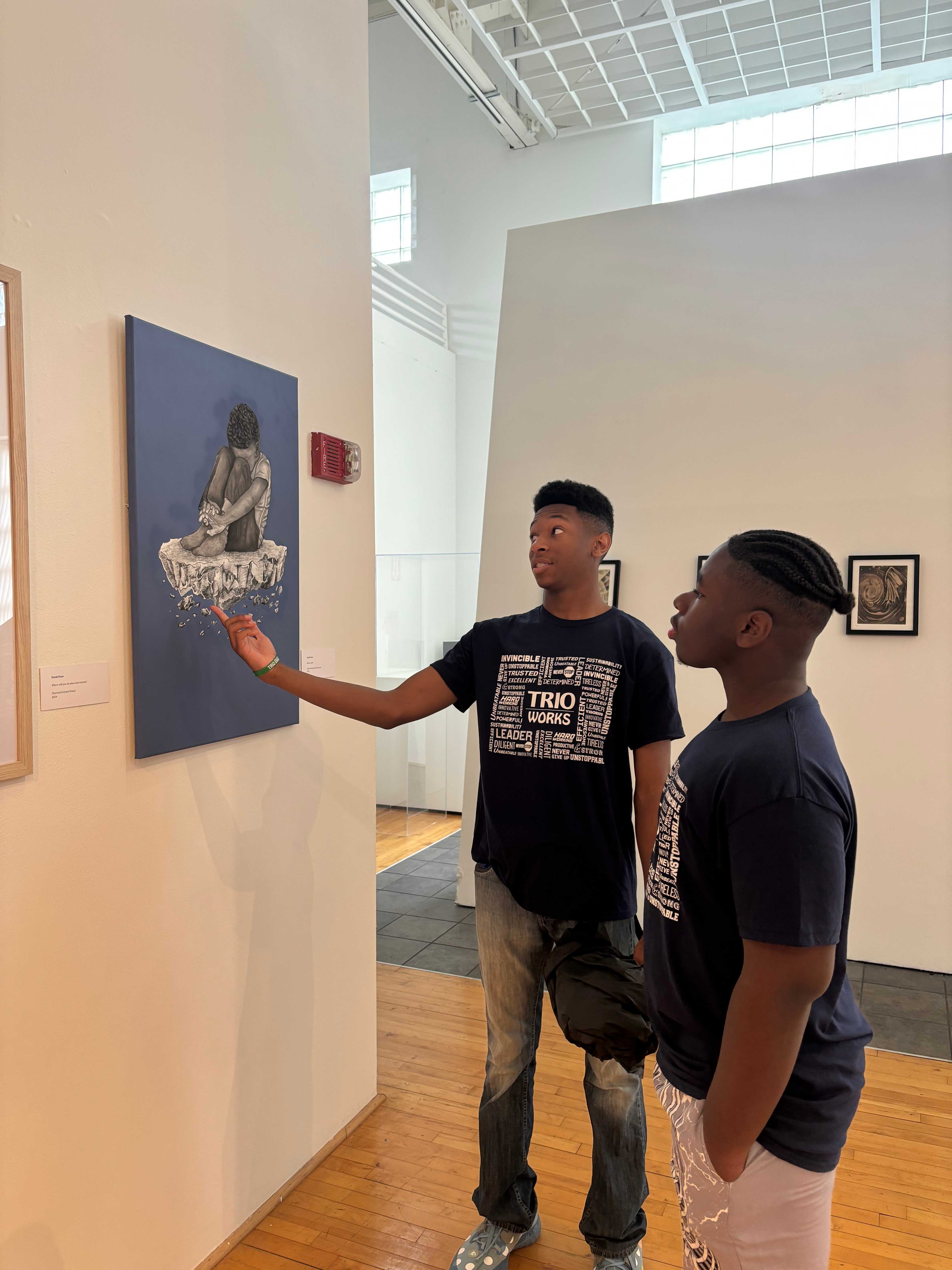 Color photo of two young men looking a painting on the wall of a gallery.