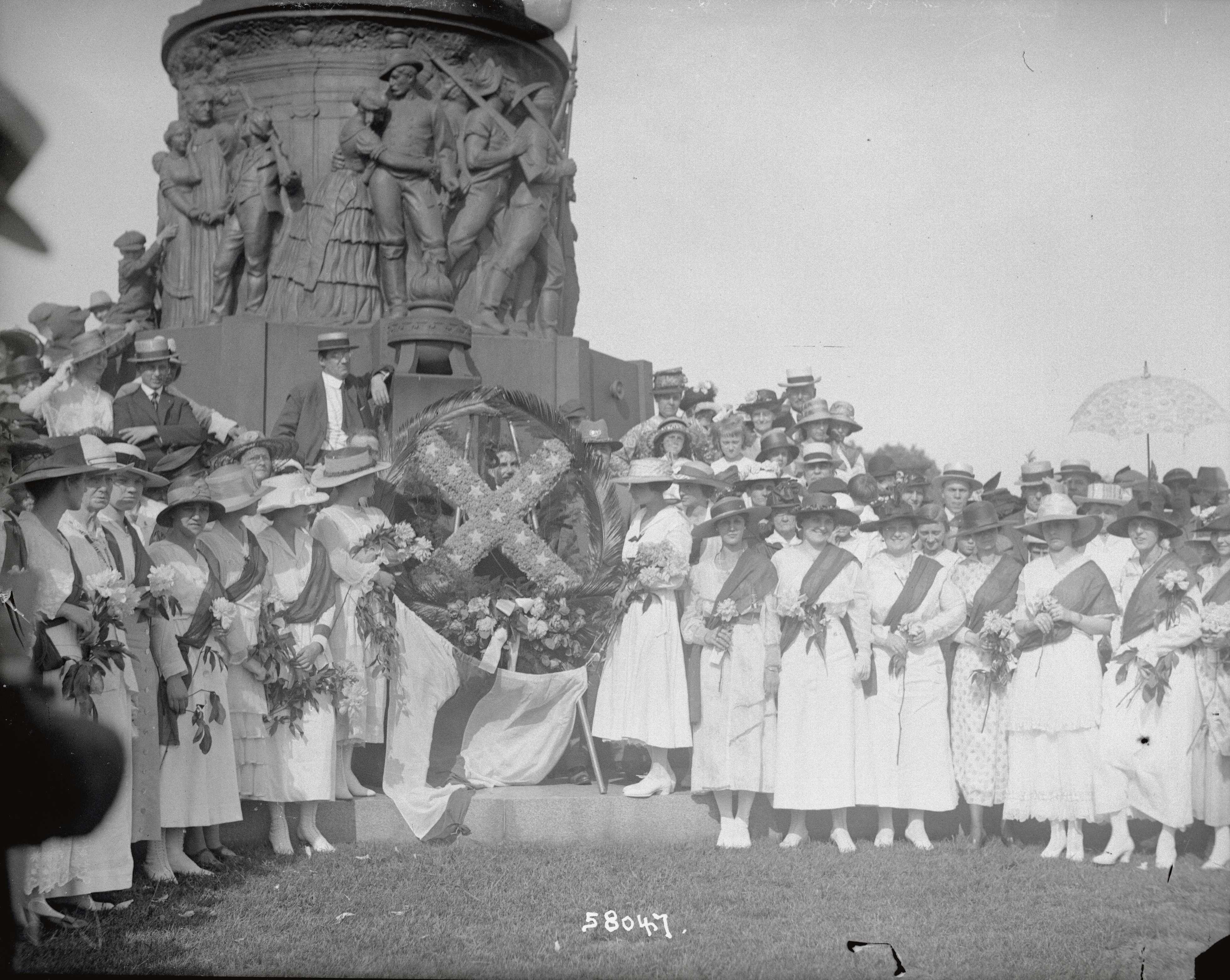 A photo of a large group of The United Daughters of the Confederacy posing together stand together in front of a monument.