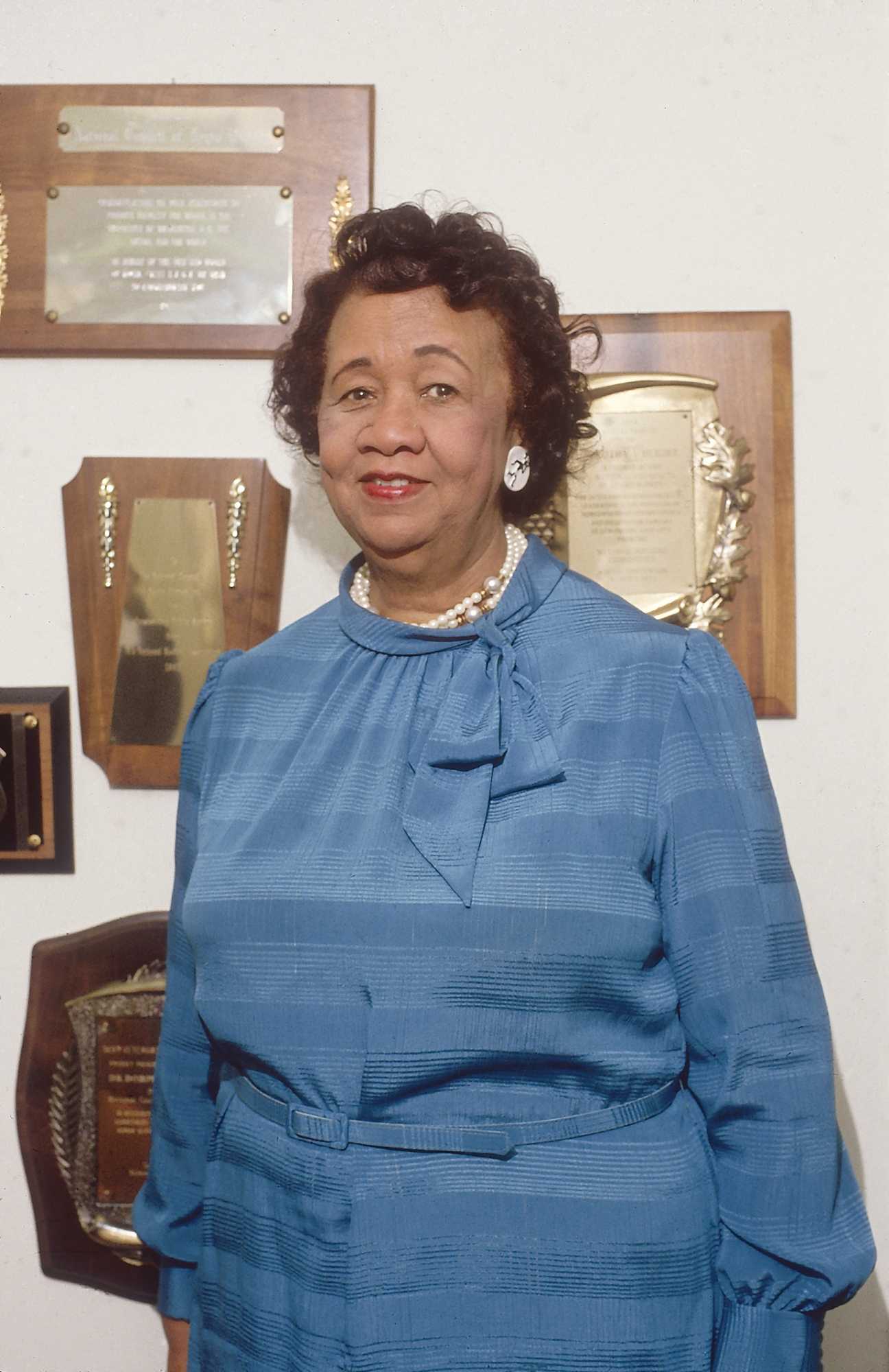 Photograph of Dr. Dorothy Height stands in front of wall plaques