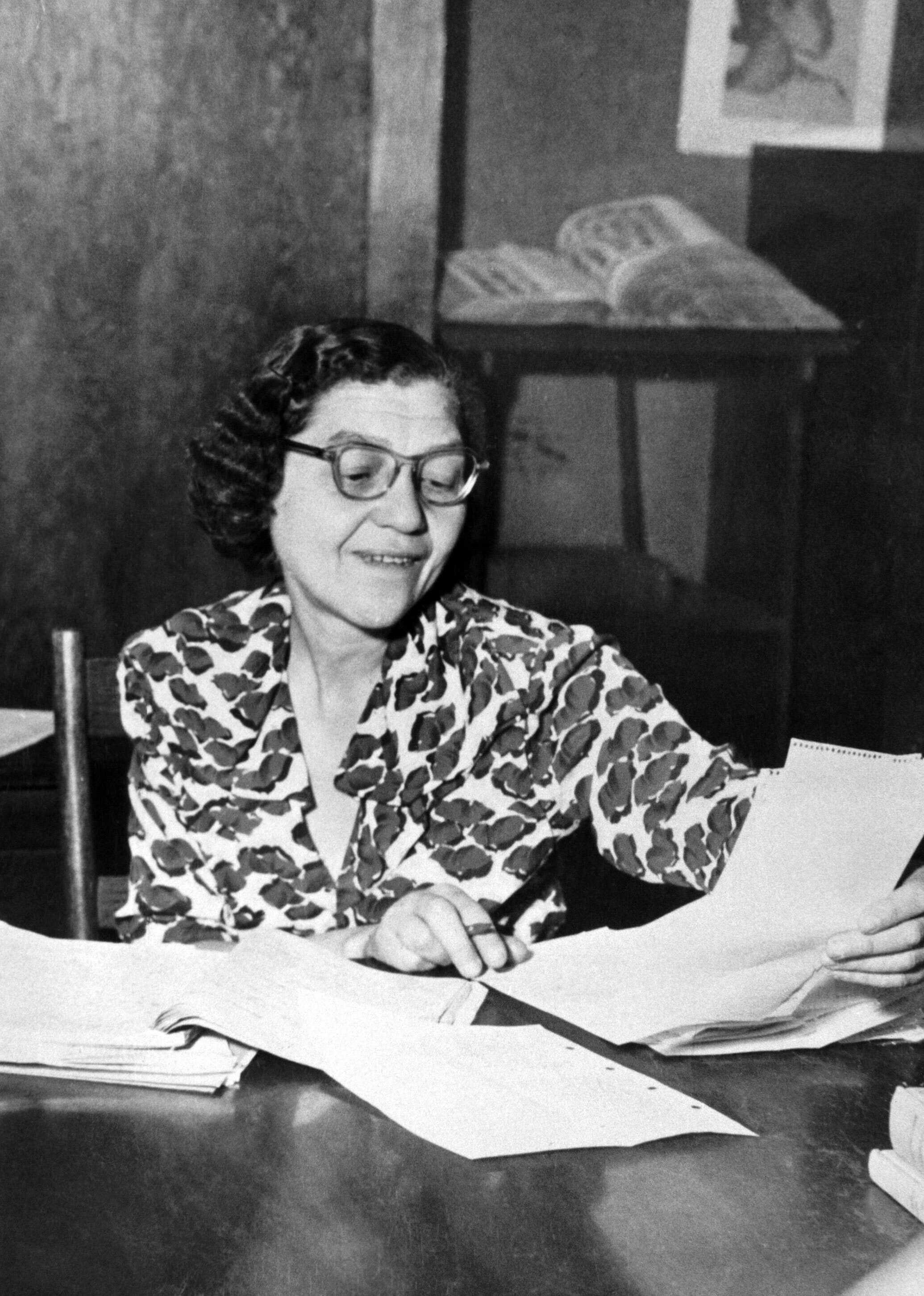 A photo of a woman sitting at a desk sorting through papers.