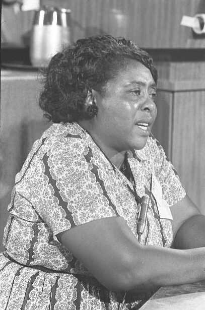 A still photograph of Fannie Lou Hamme talking, sitting at a kitchen table.