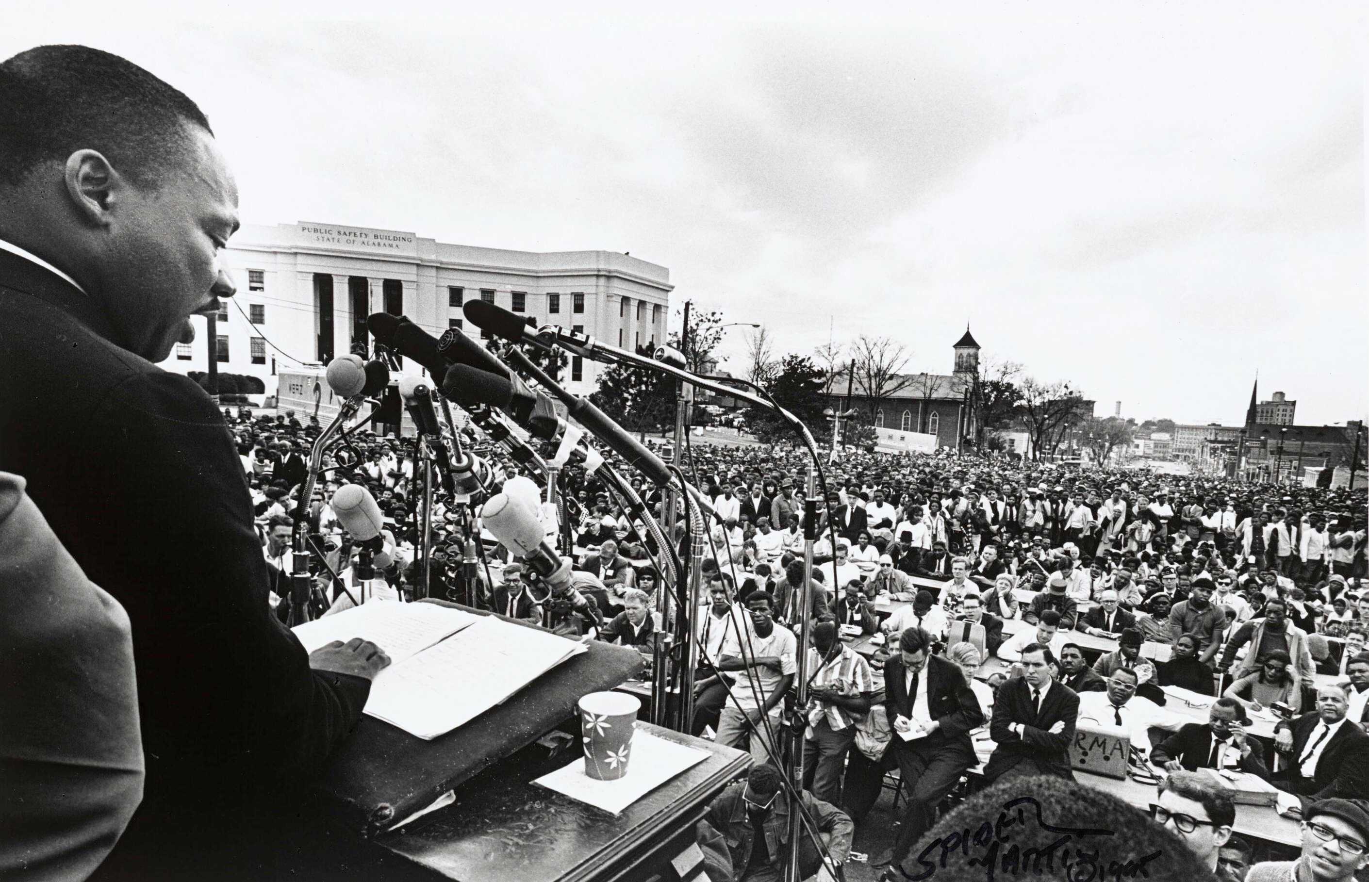A black-and-white photograph of Martin Luther King. Jr. delivering a speech in Montgomery, Alabama.