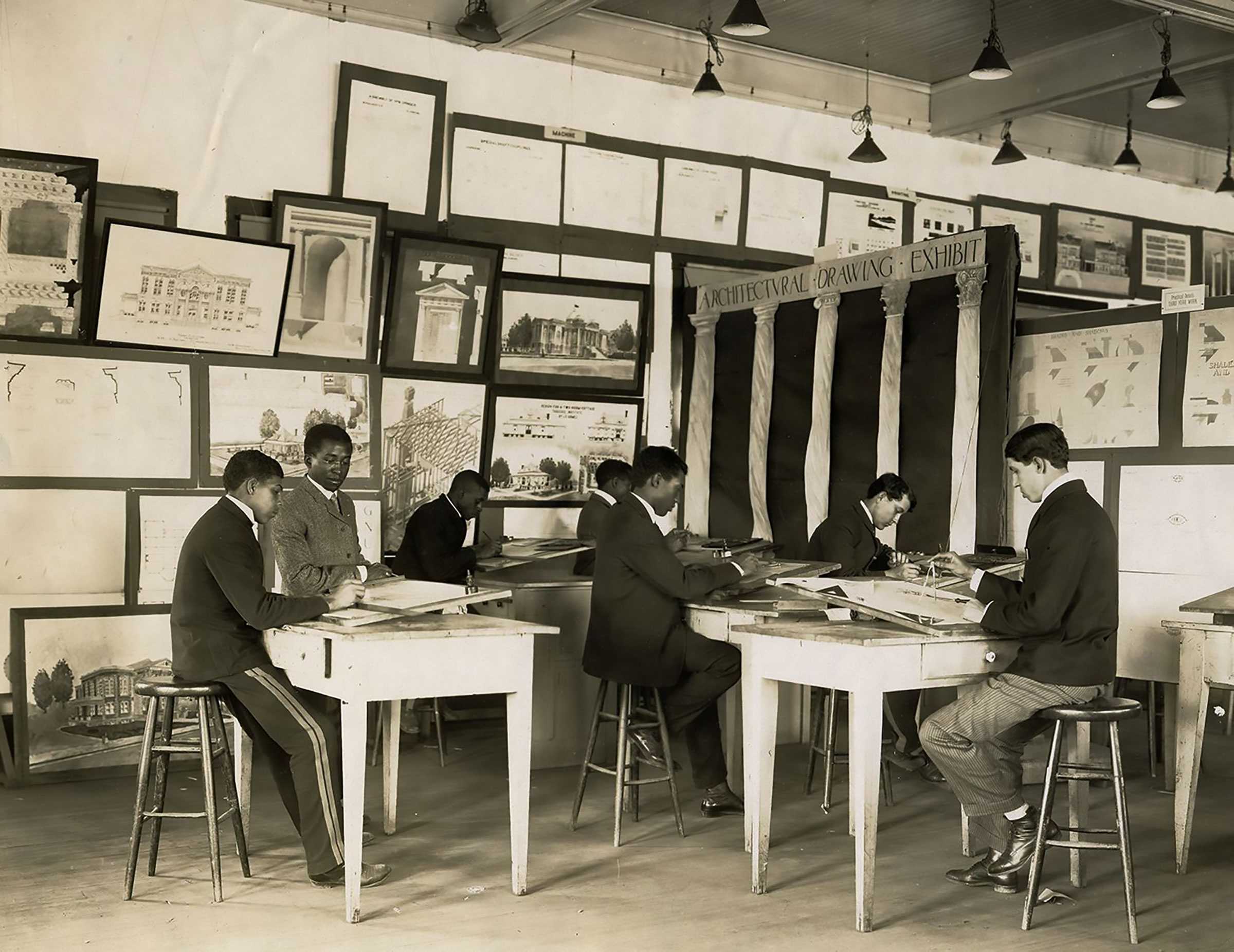 Photo of students working at desks in an architectural drawing class, with drawings displayed on the walls.