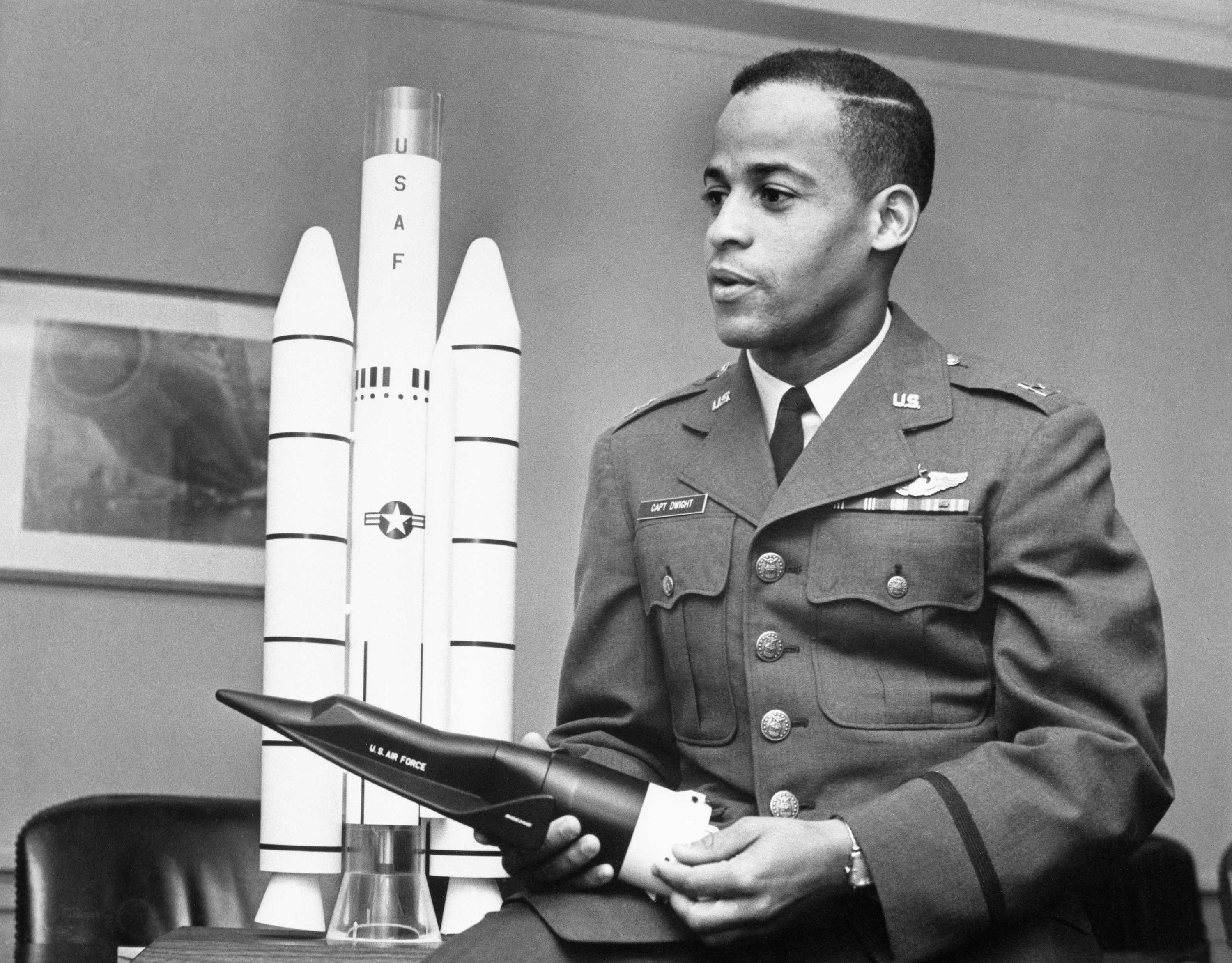 A black and white photo of Captain Dwight Jr. sitting on a desk holding a model U.S Air force plane in his hand.