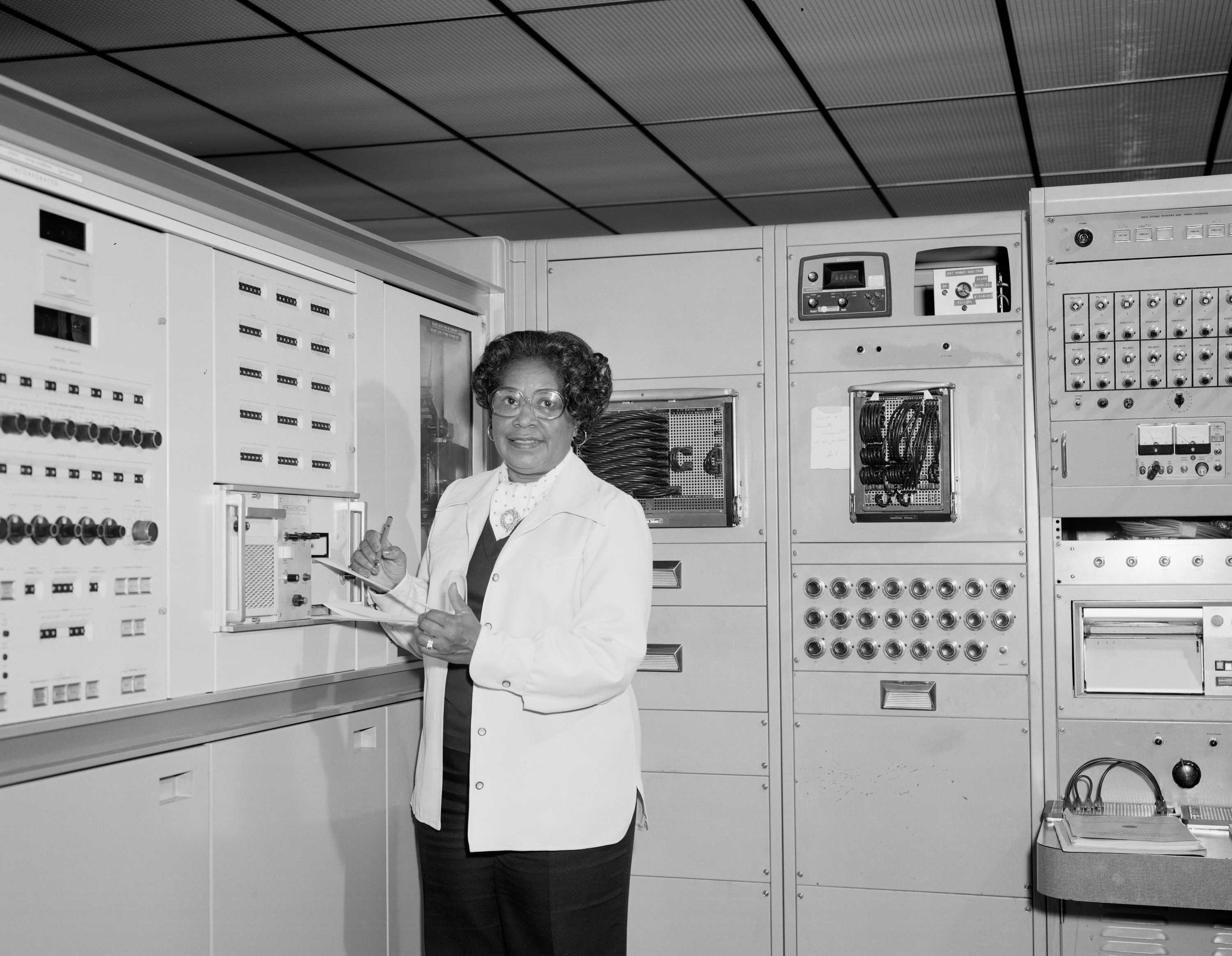 Mary Jackson is smiling at the camera as she poses for a black and white photo. She has a clipboard in her hand.