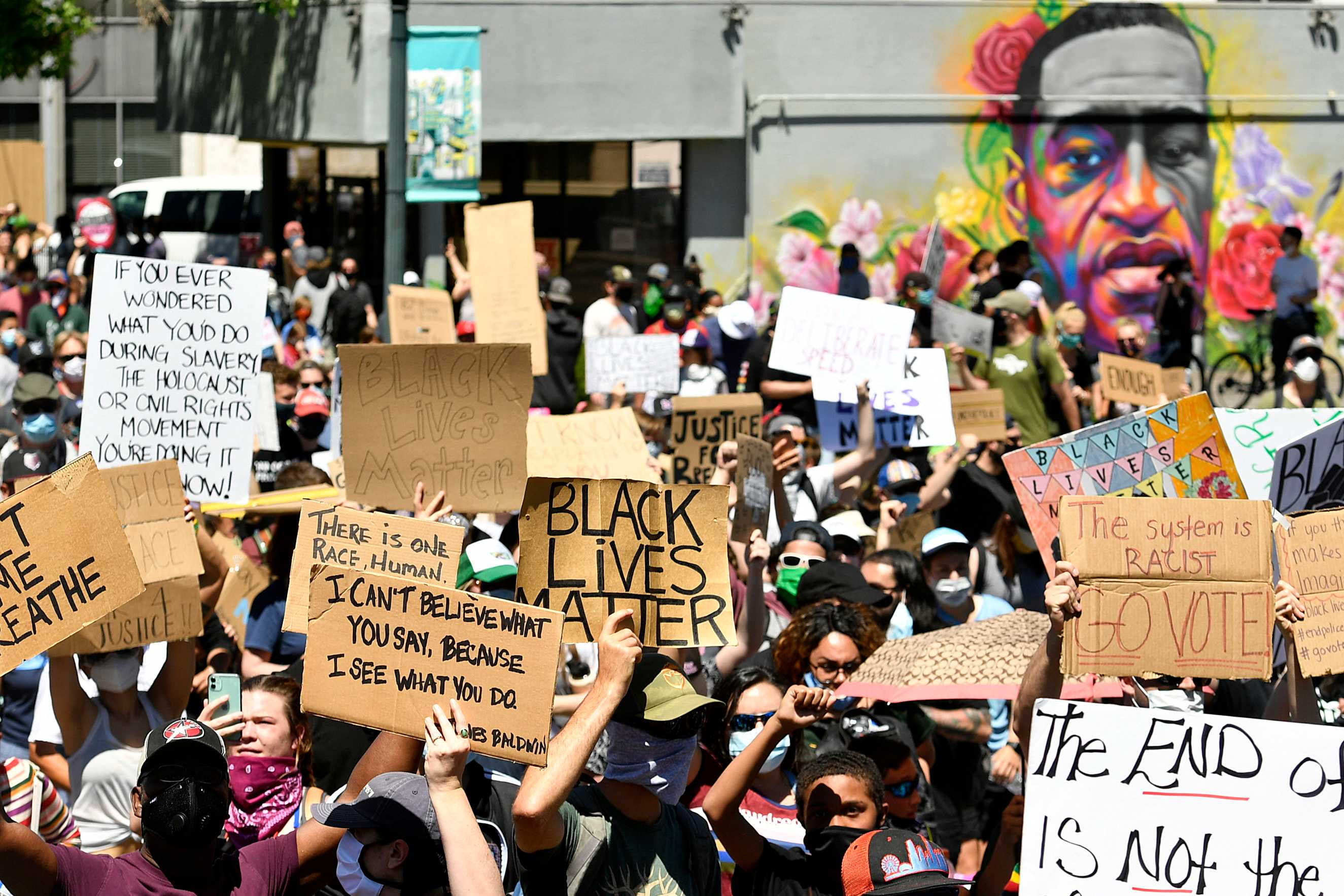 Photograph of marchers walking past a mural of George Floyd