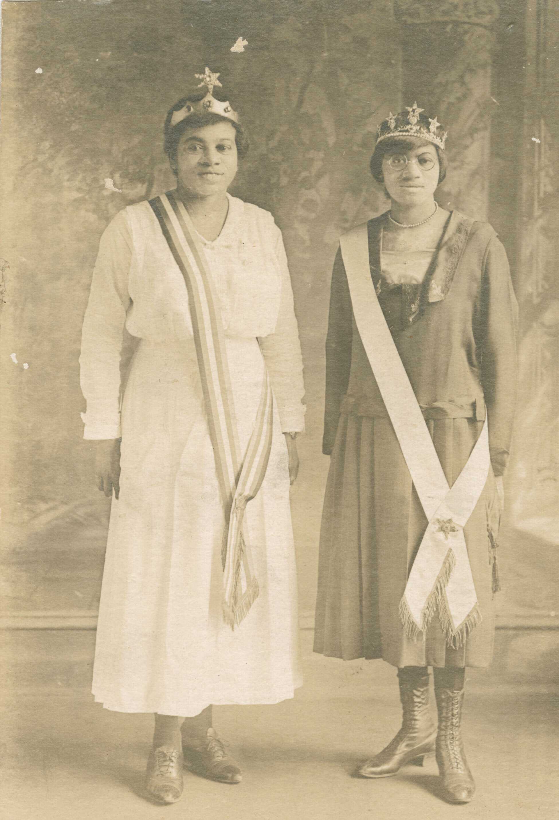 Black and white photographic postcard of Magdalene Hendricks (right) and her sister (left) wearing tiaras and sashes across their right shoulders.