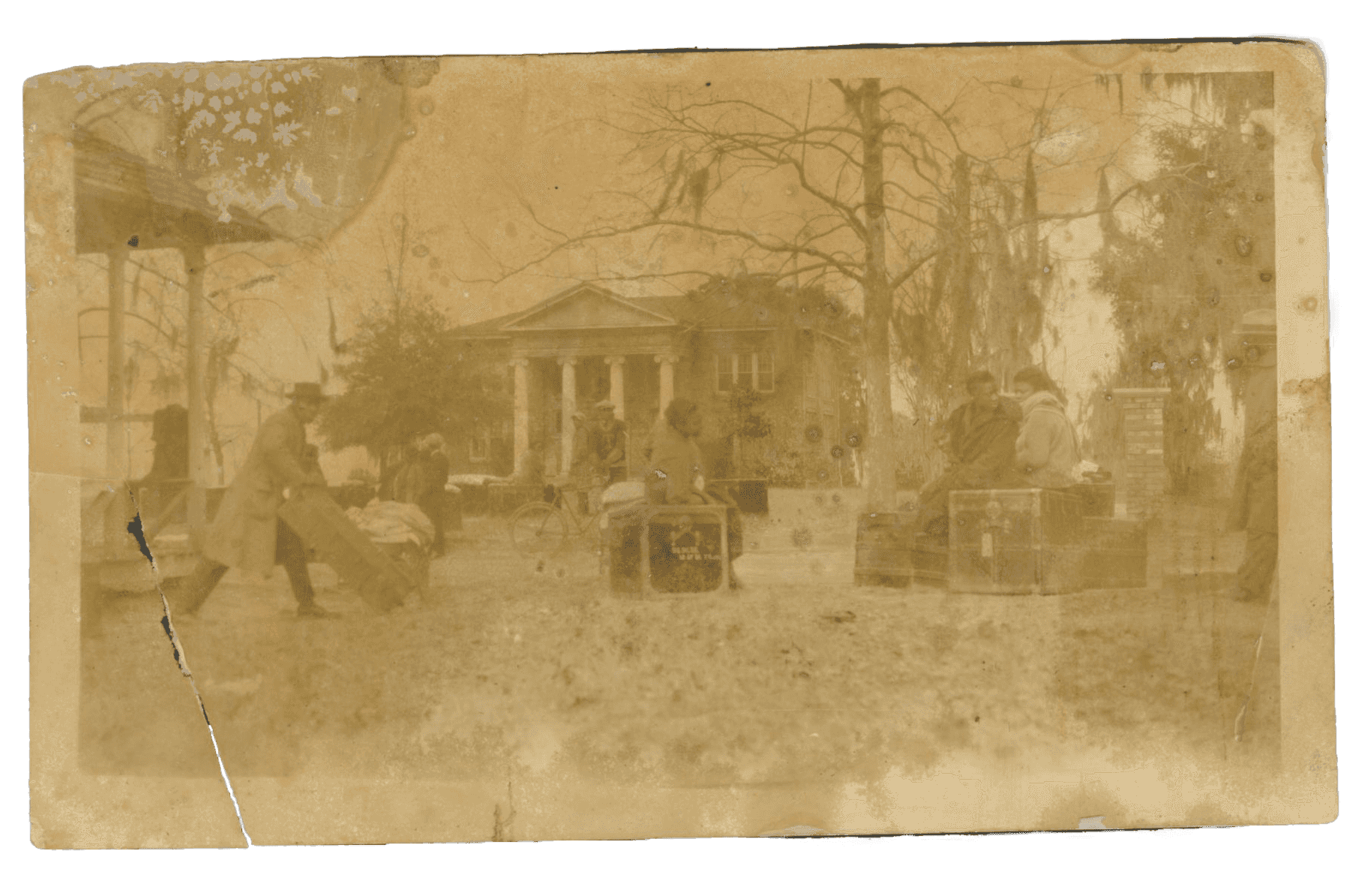 A black and white photo of people sitting on storage trunks in front of a building with columns.