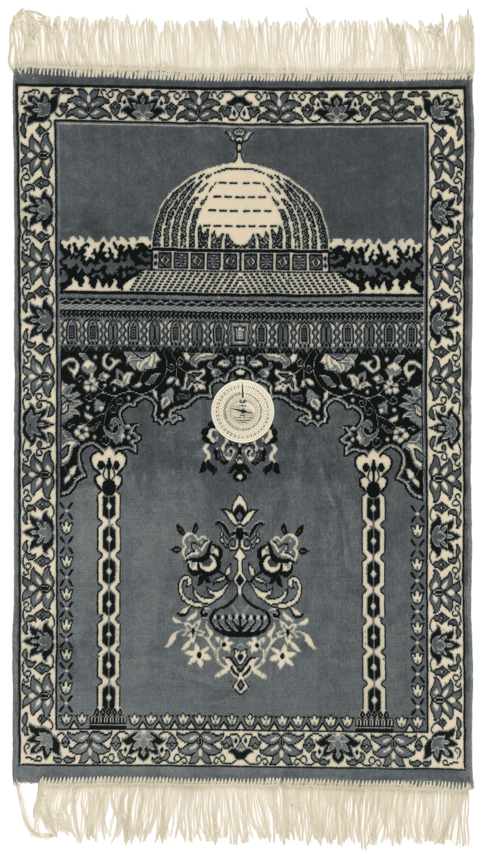 The prayer rug is a low-pile carpet with a primarily gray-blue background with black and white design details. The design featured in the top third of the rug is the image of an architectural dome with a small floral spire at the top. Below the dome is a geometric pattern running horizontally across the rug. Below the geometric pattern in the lower two-thirds of the rug is a stylized architectural interior with geometric columns on either side of the space. At the top of the columns is a stylized arch of floral and scalloped patterns. At the top of the arch, attached to the rug, is a white plastic compass. The compass is a Qibla directional compass. Below the compass needle, at the bottom, is the manufacturer information [HILAL / Tel. 069-28 77 69 / Praying carpets / W.-Germany]. Below the compass, in the center, is a floral motif. Surrounding the edges of the rug is a border with a floral pattern. At the top and bottom of the rug is white fringe.