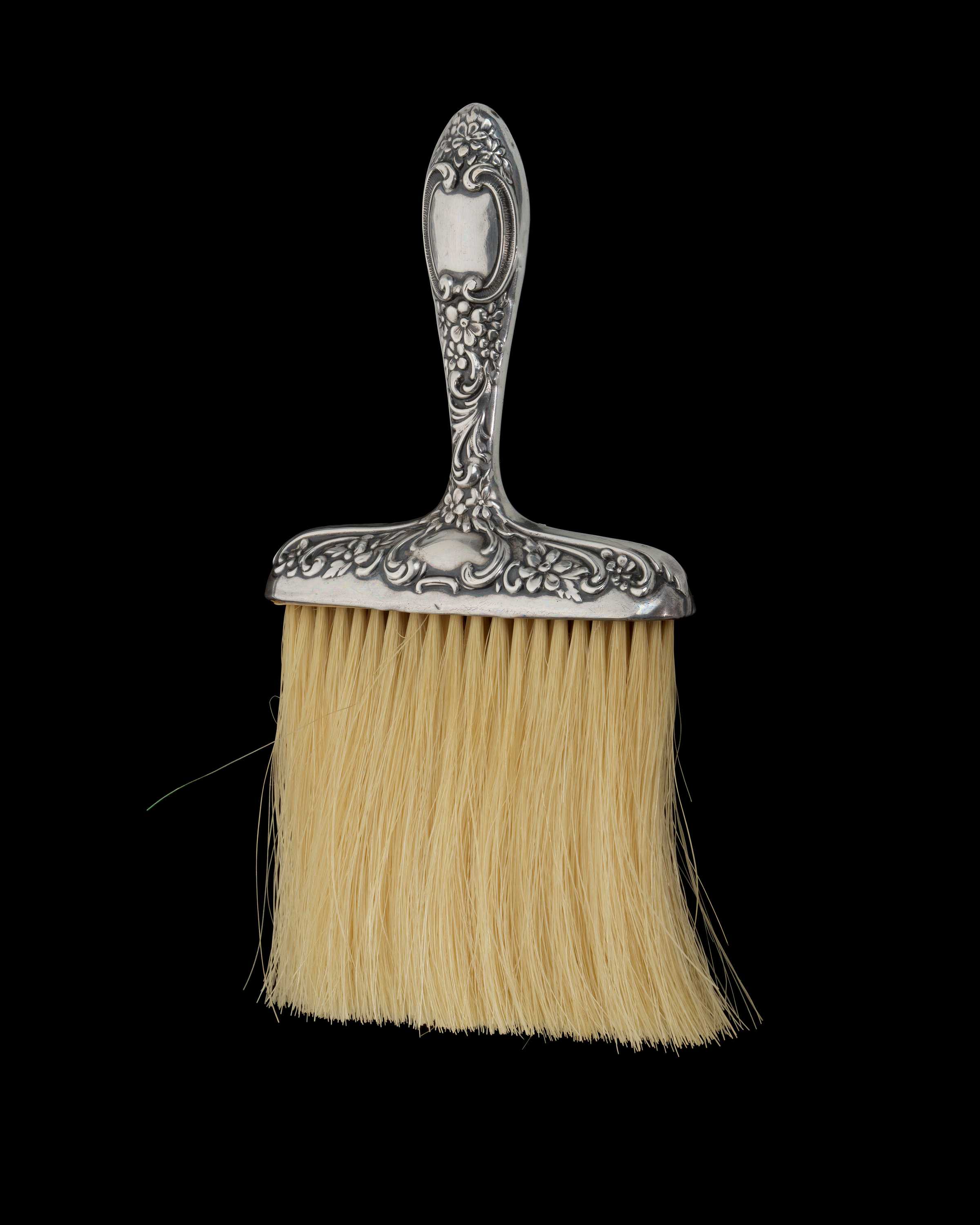 Silver whisk brush with yellow bristles.  The silver handle has decorative scrollwork throughout.