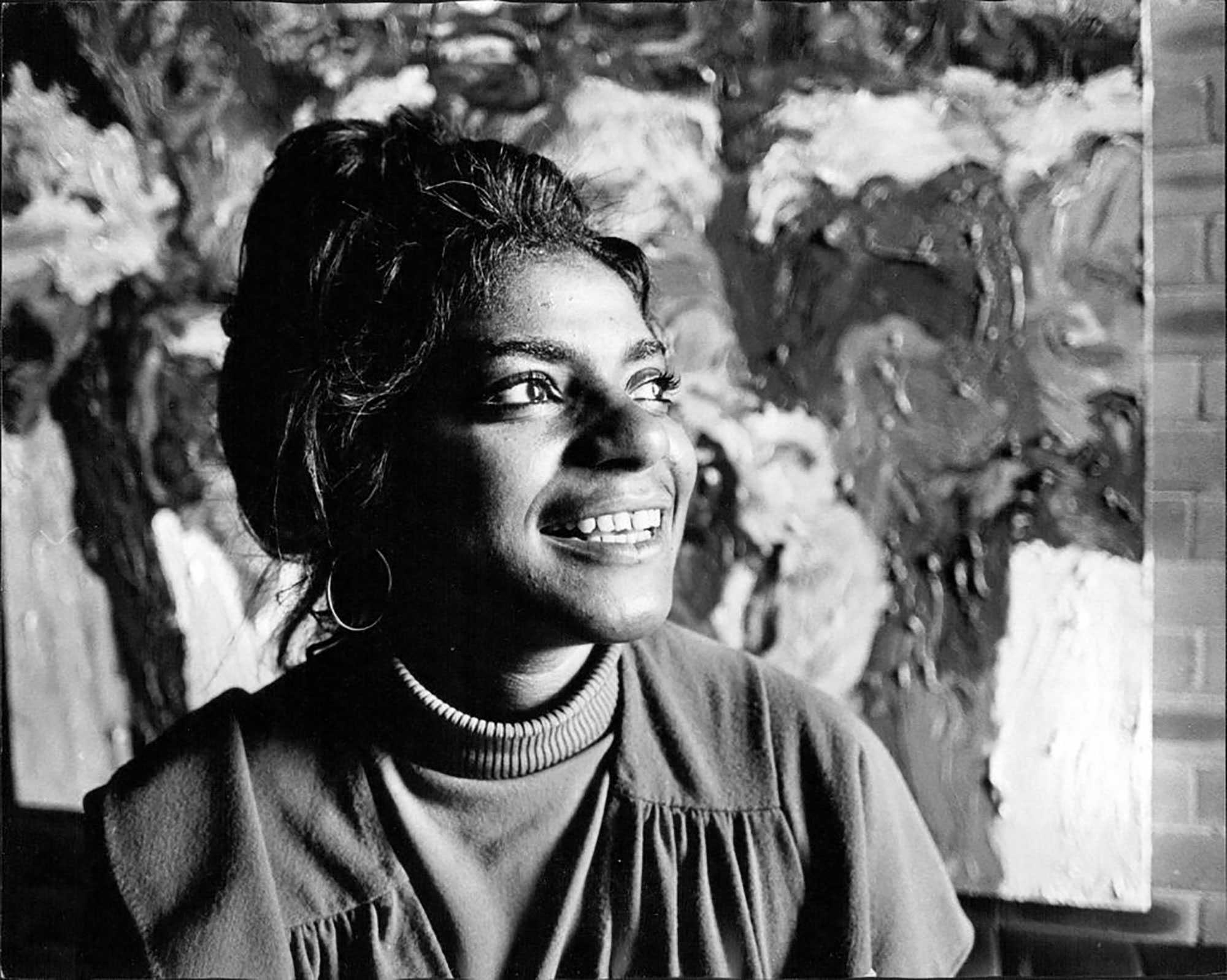 Black-and-white photo of a smiling woman in front of an abstract painting.