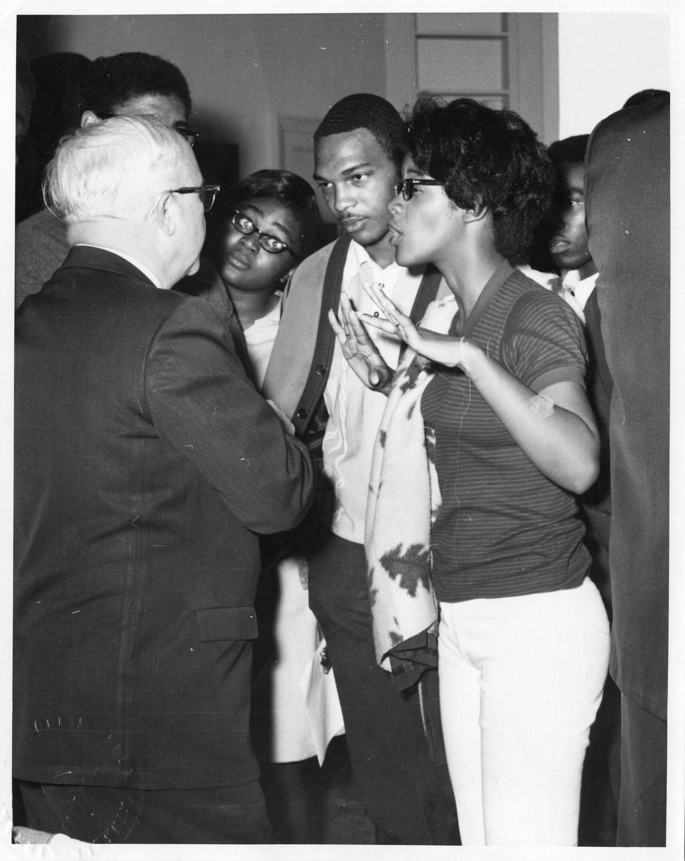 A black and white photos of people speaking with each other.