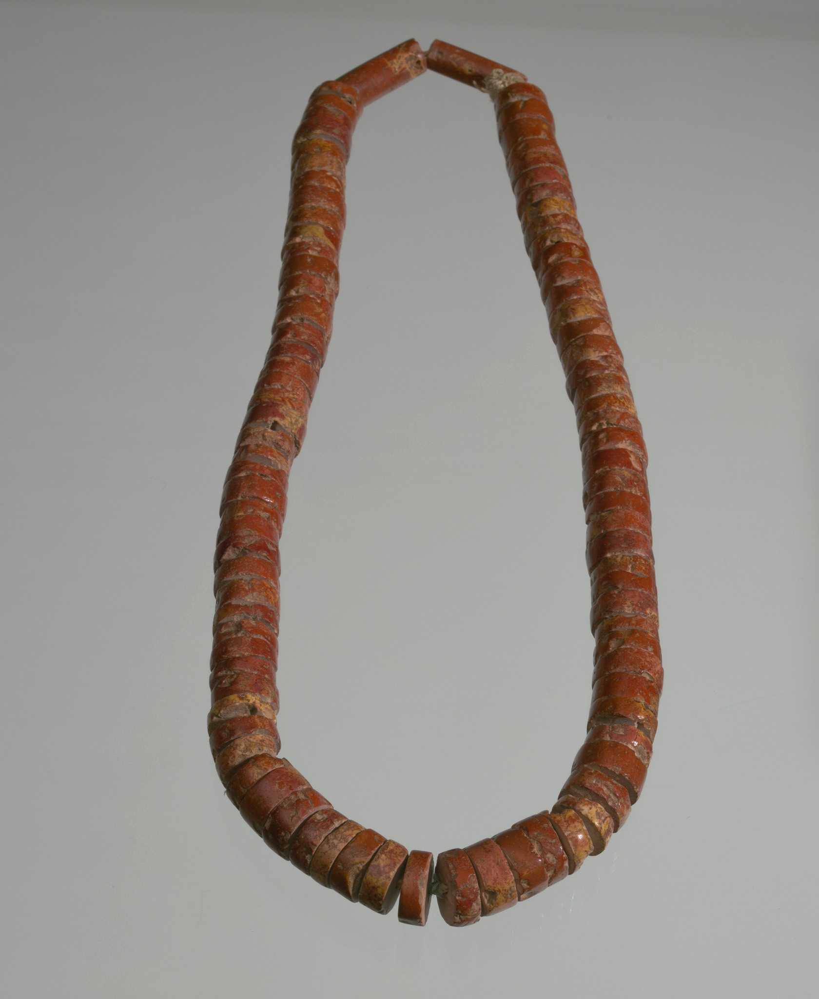 A looped strand of red colored beads on display against a grey background.