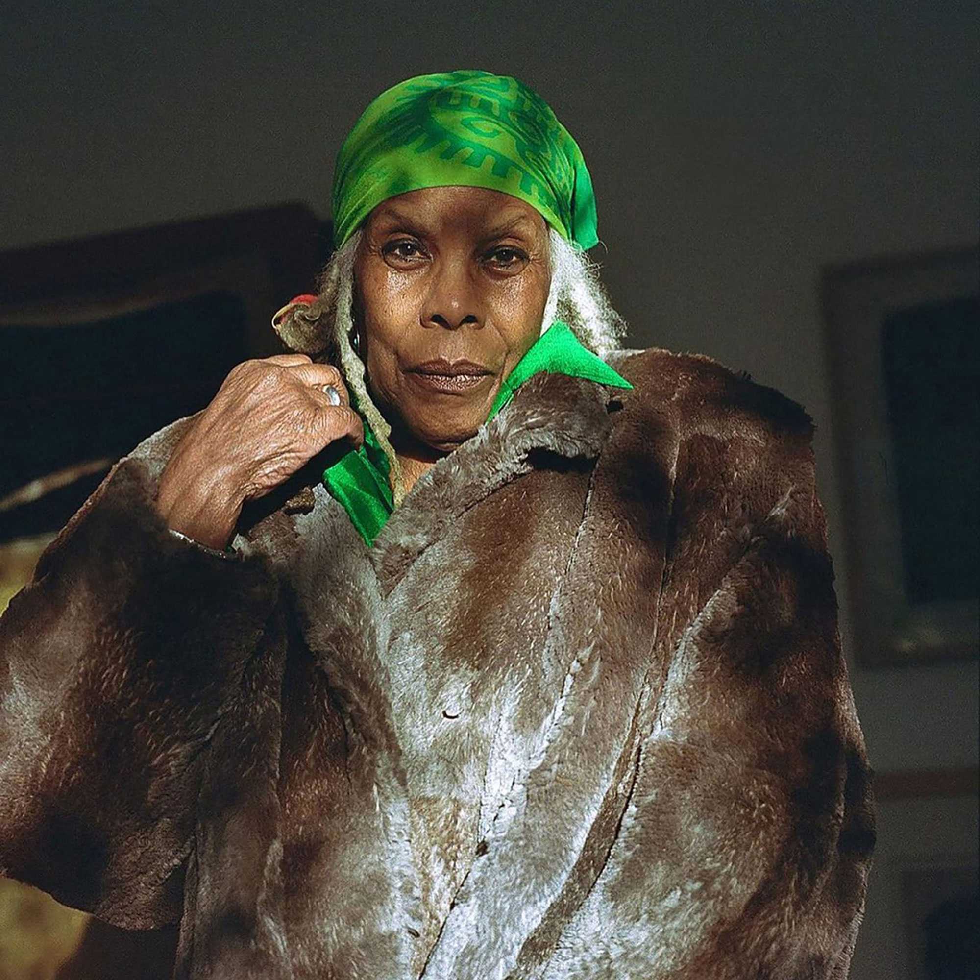 Portrait of a person wearing a fur coat and a green headscarf.