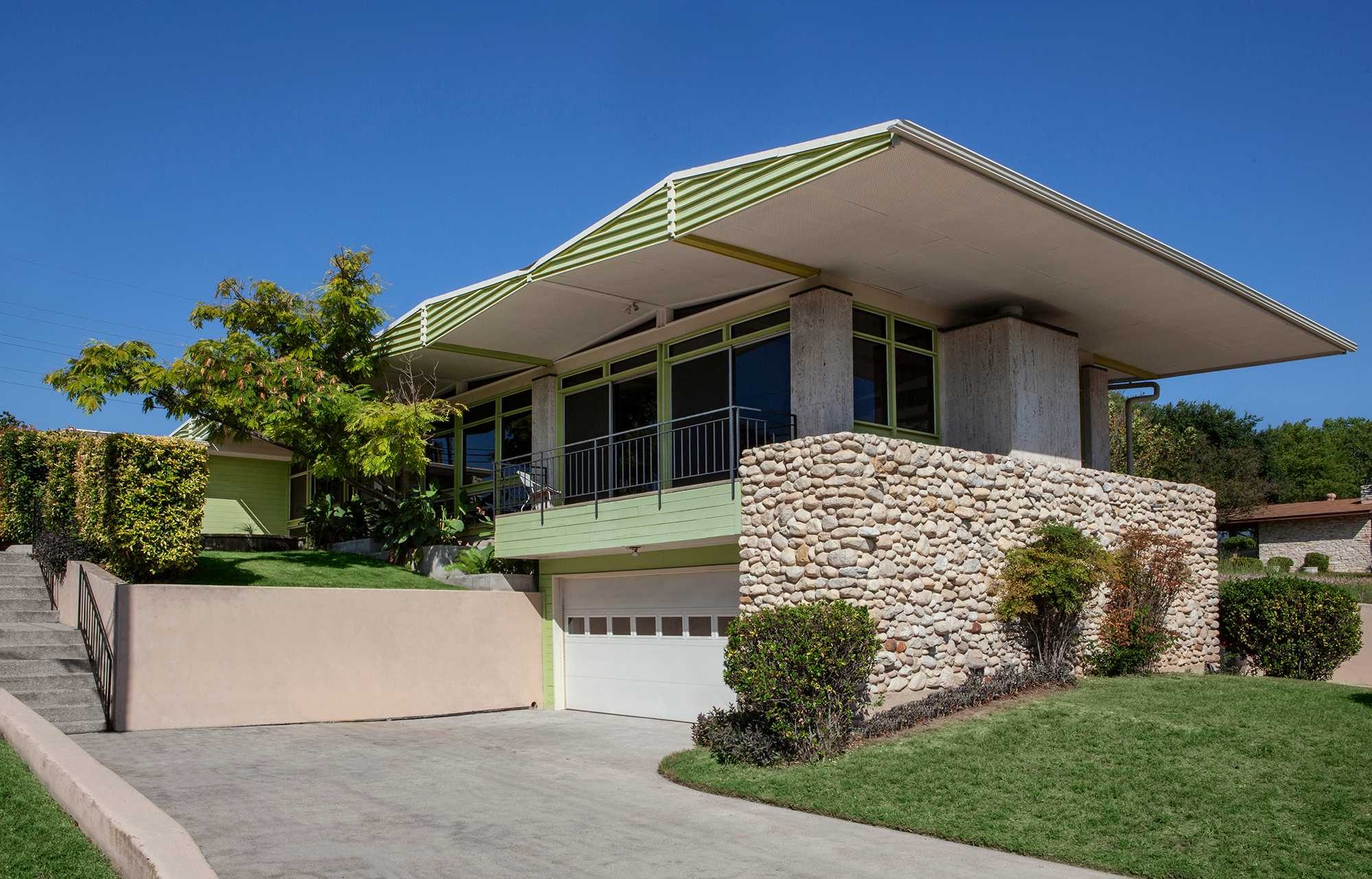 Modern single-story house with flat roof, stone accents, large windows, and landscaped yard.