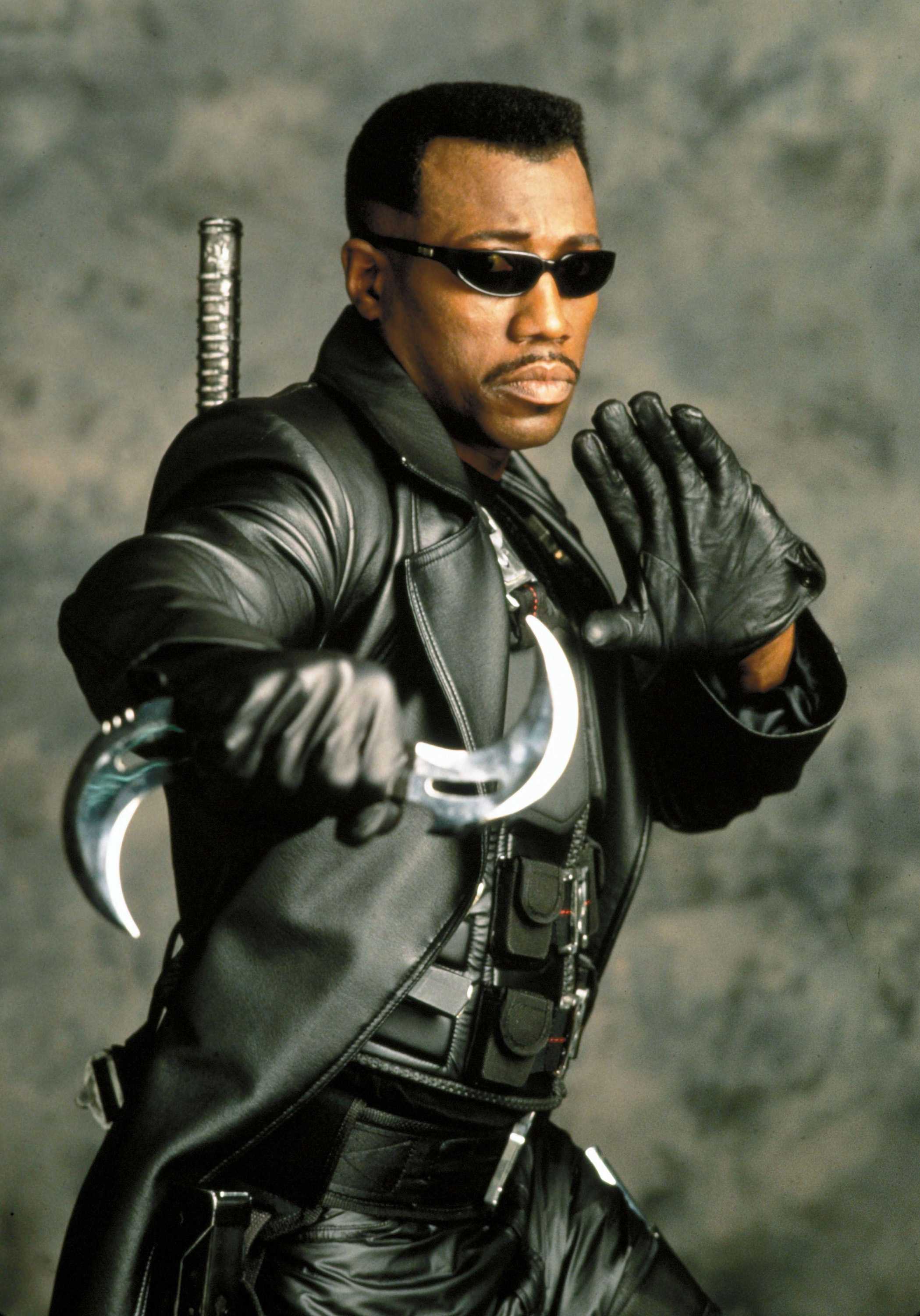 Wesley Snipes, as Blade, poses ready for action. He is dressed in all black and has small cuved blade in his hand.