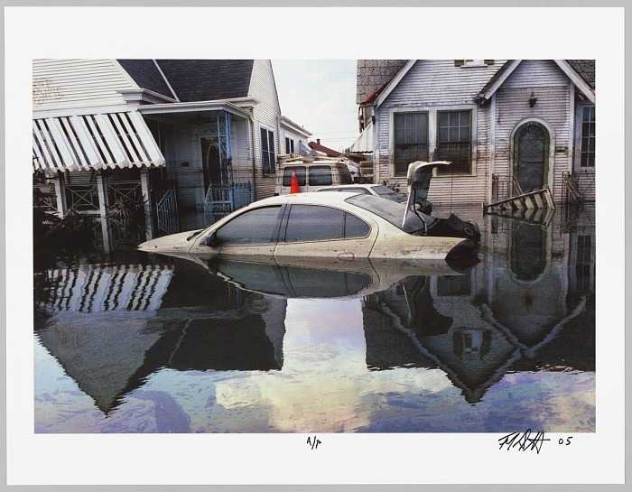 A color photograph of flooding in New Orleans after Hurricane Katrina. At center is a car, a four door sedan with its trunk open, abandoned in water up to the door handles.