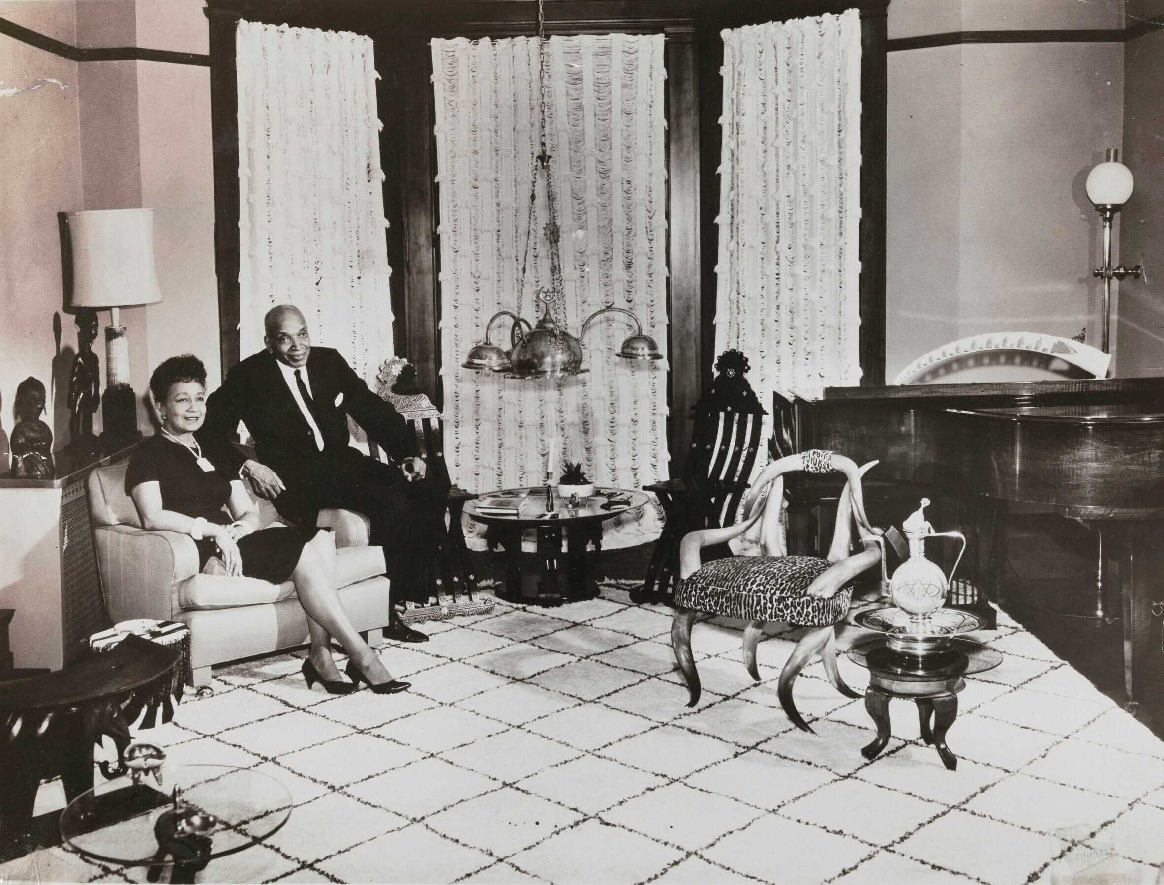 Black and white photograph of woman and a man seated next to each other in a highly decorated room.