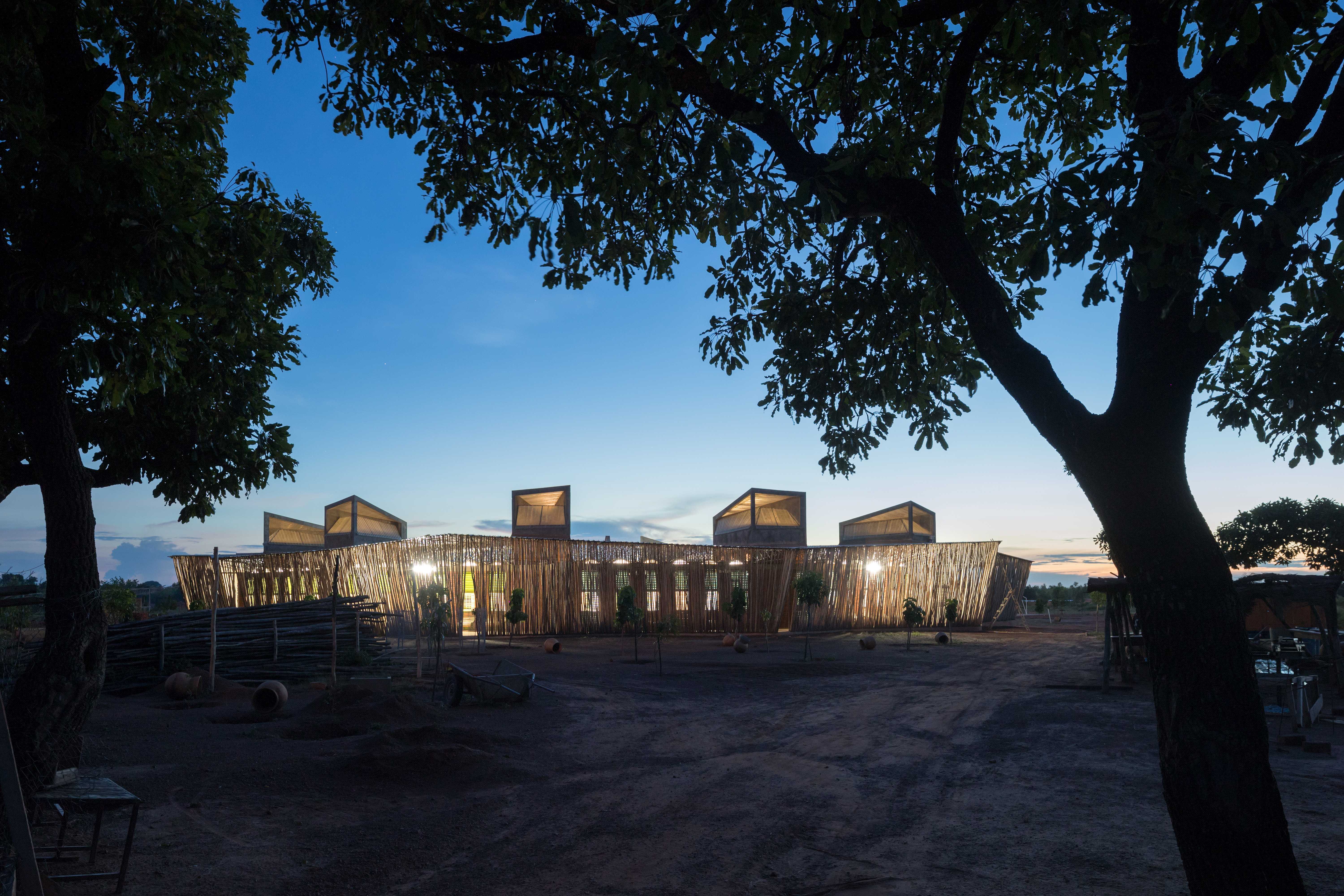 A landscape view of Lycée Schorge Secondary School at dusk. The school's is dimily light within.