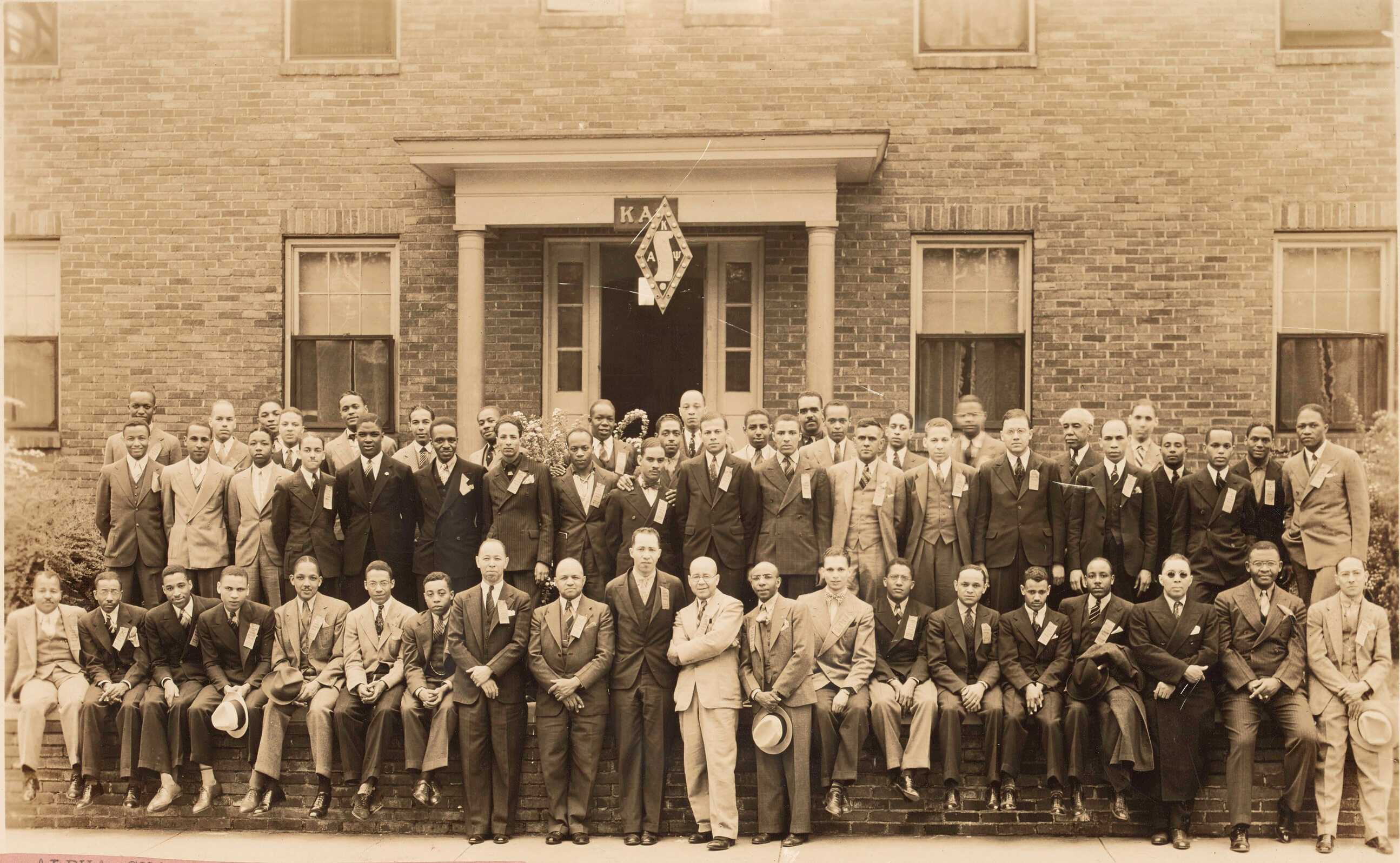 This black and white photograph depicts members of the Kappa Alpha Psi fraternity in front of the Alpha Chapter house during the North Central Province regional meeting.