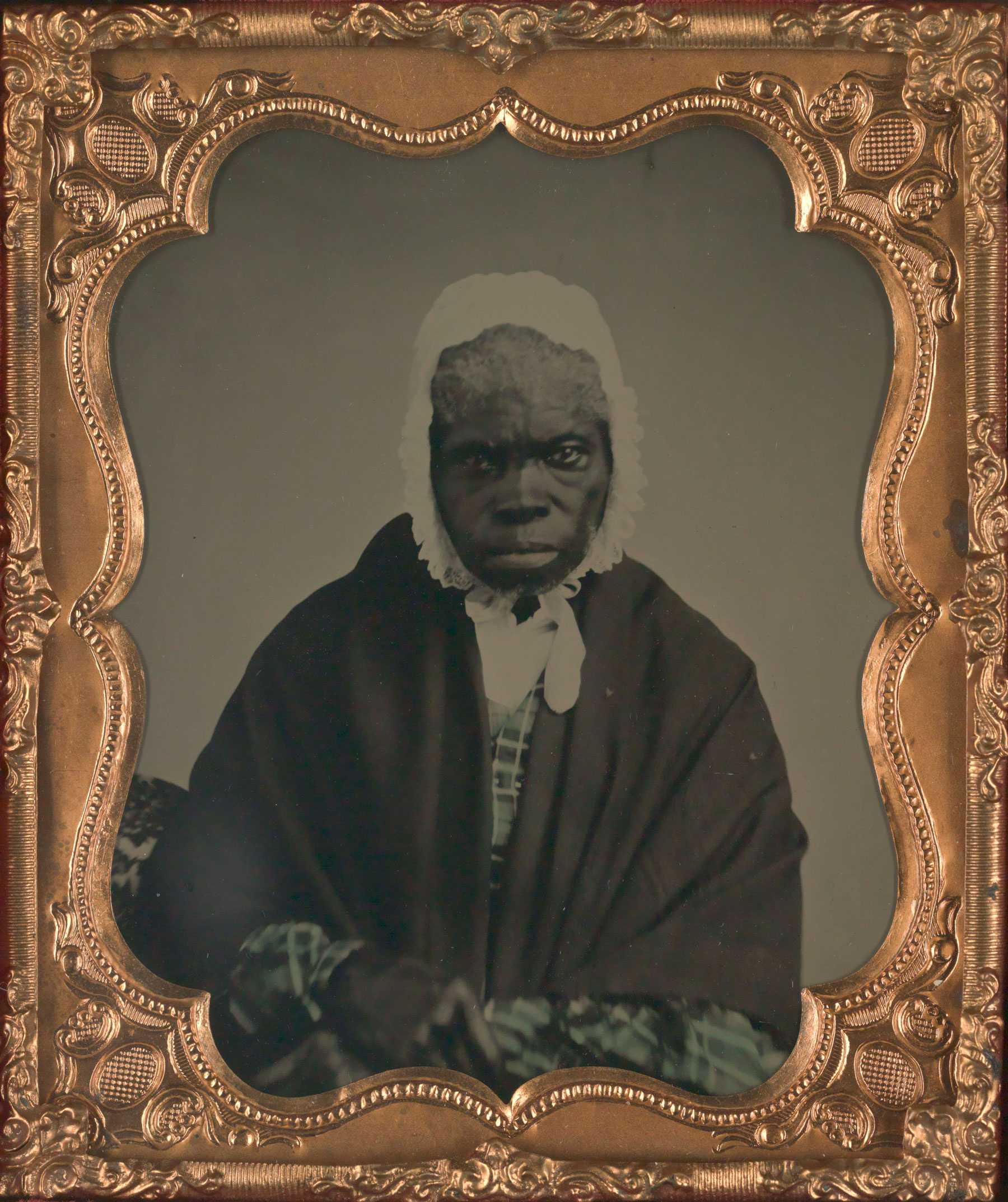 Photograph of a woman wearing a bonnet and shawl, set in an ornate gold frame.