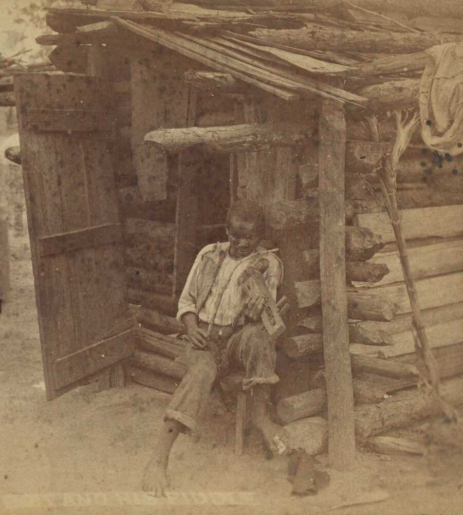 A stereograph titled "Bob and His Fiddle" printed and photographed by O. Pierre Havens of Savannah, Georgia. The albumen prints depict a boy holding a homemade fiddle while seated outside a small log dwelling. He wears a white shirt, dark vest, dark pants, and no shoes. His hat is lying on the ground by his left foot. He looks down at the fiddle held in his left hand and propped on his left shoulder, while holding a bow made from string and a bent stick in his right hand over the strings of the fiddle. The title is blurred and printed in the bottom left corner on the right facing print. The prints are mounted on card stock that is orange on the recto and light pink on the verso. On the verso black text in various decorative fonts reads: [Havens / (Successor to Wilson & Havens) / PHOTOGRAPHER / 141 & 143 Broughton Street / SAVANNAH, GA. / PUBLISHER OF THE / LARGEST COLLECTION / OF / SOUTHERN VIEWS / IN / THE UNITED STATES.].