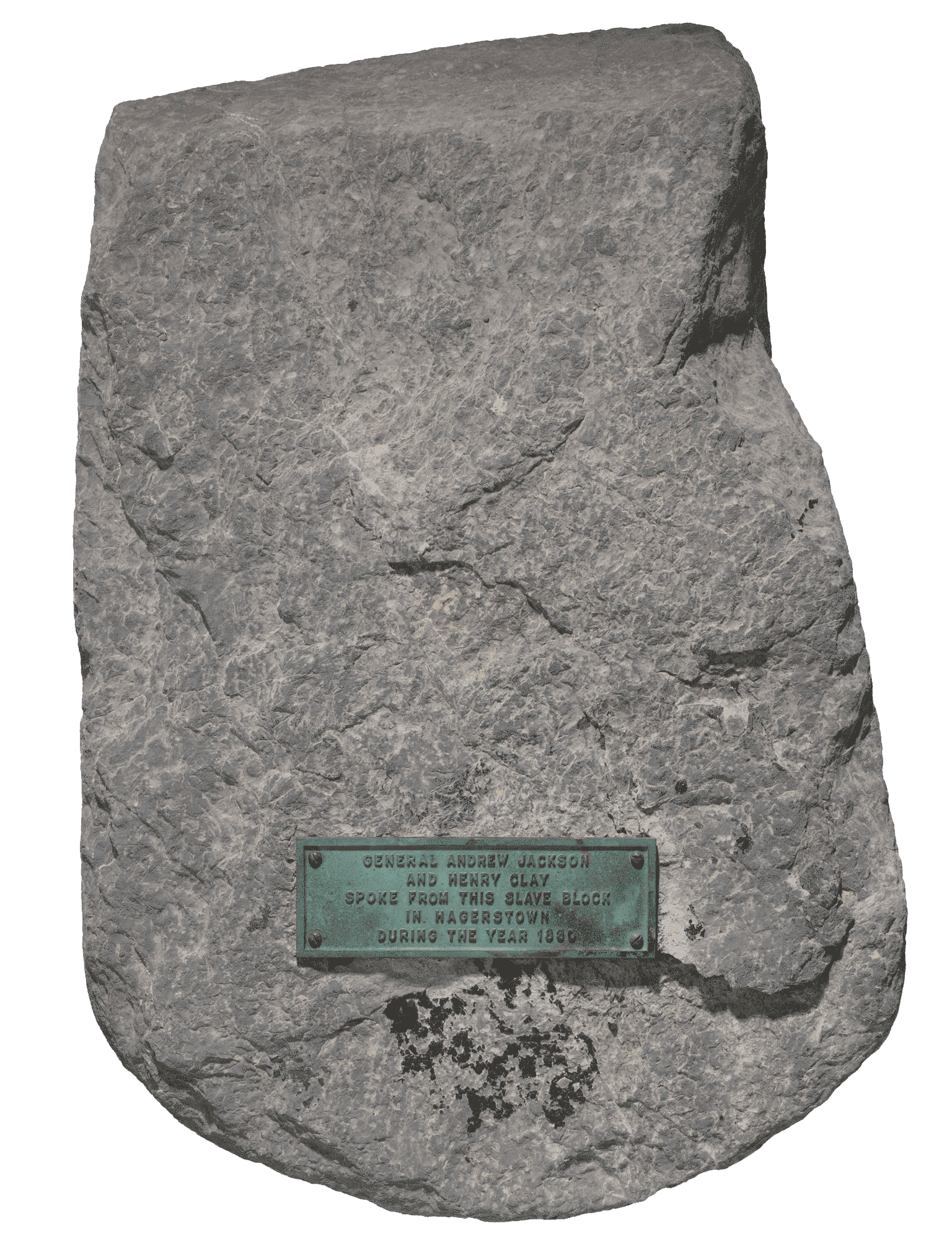 A large gray carved marble Calc-silicate shist stone with a flattened top and bottom, squared back and sides, and a rounded front used as a slave auction block in Hagerstown, Maryland. A rectangular metal plaque is screwed to the top of the stone, with embossed text reading “GENERAL ANDREW JACKSON / AND HENRY CLAY / SPOKE FROM THIS SLAVE BLOCK / IN HAGERSTOWN / DURING THE YEAR 1830.”