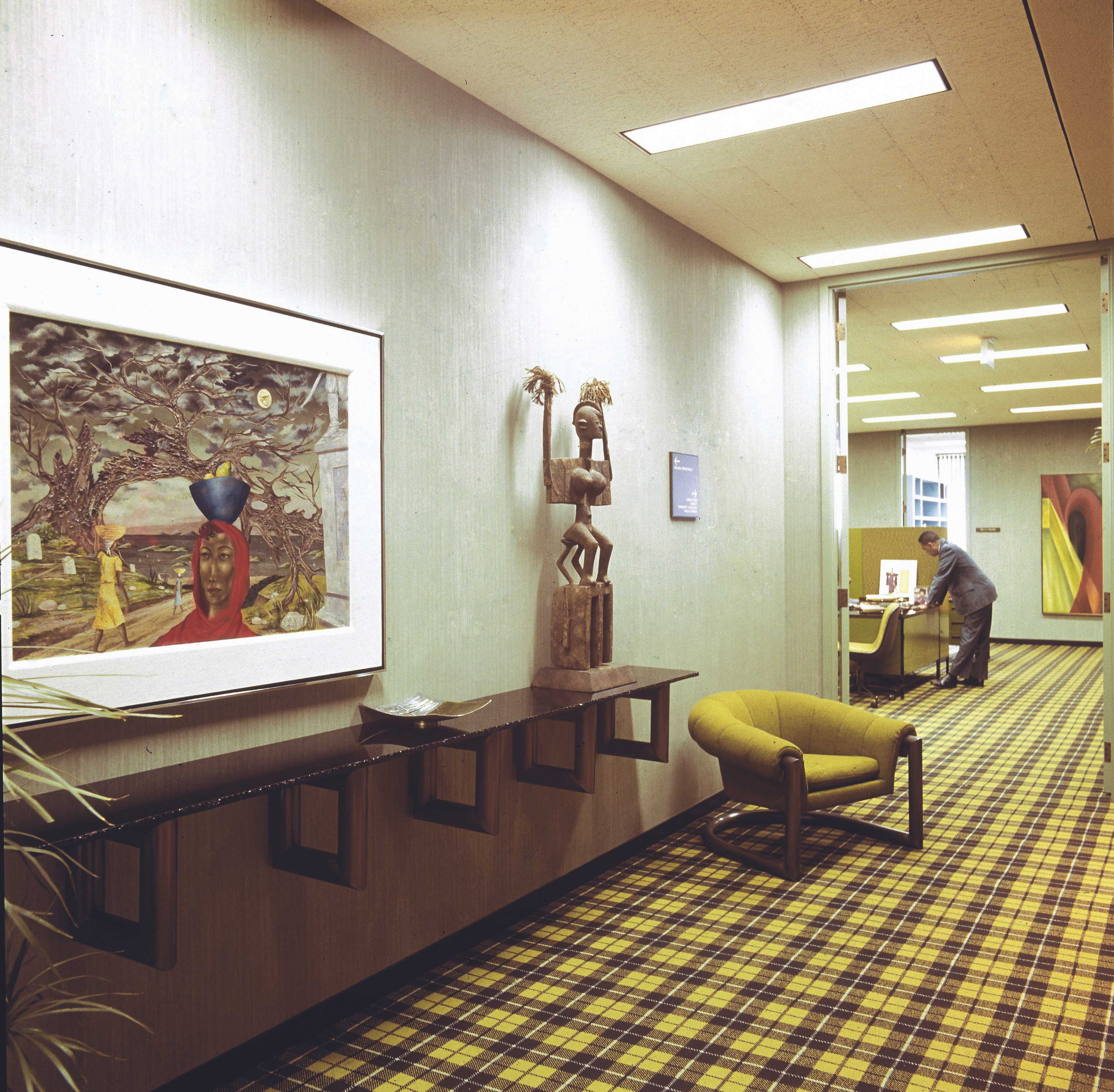 A photos of a 70s office with yellow and black patterned carpet and African art on the walls.