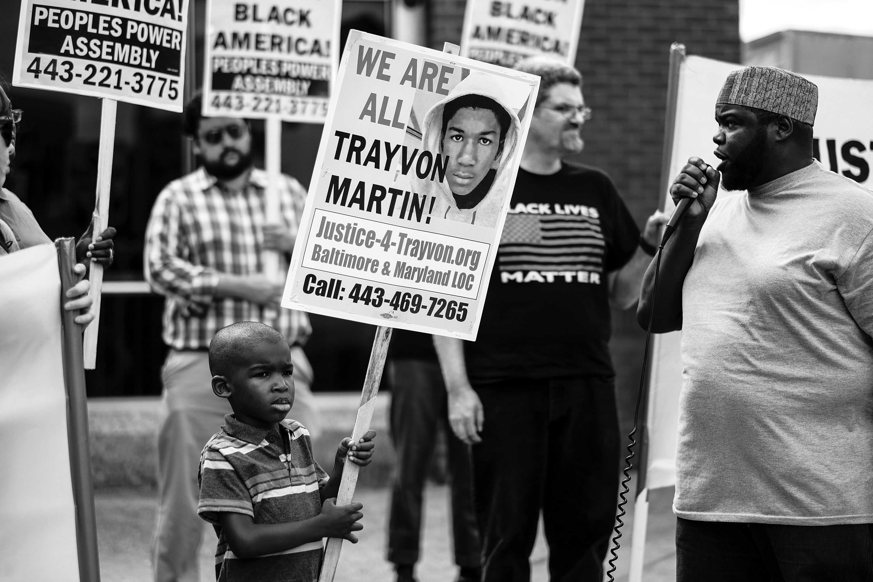 A young boy, probably around 5 years old, is holding a Trayvon Martin picking sign among a crowd of protestors.