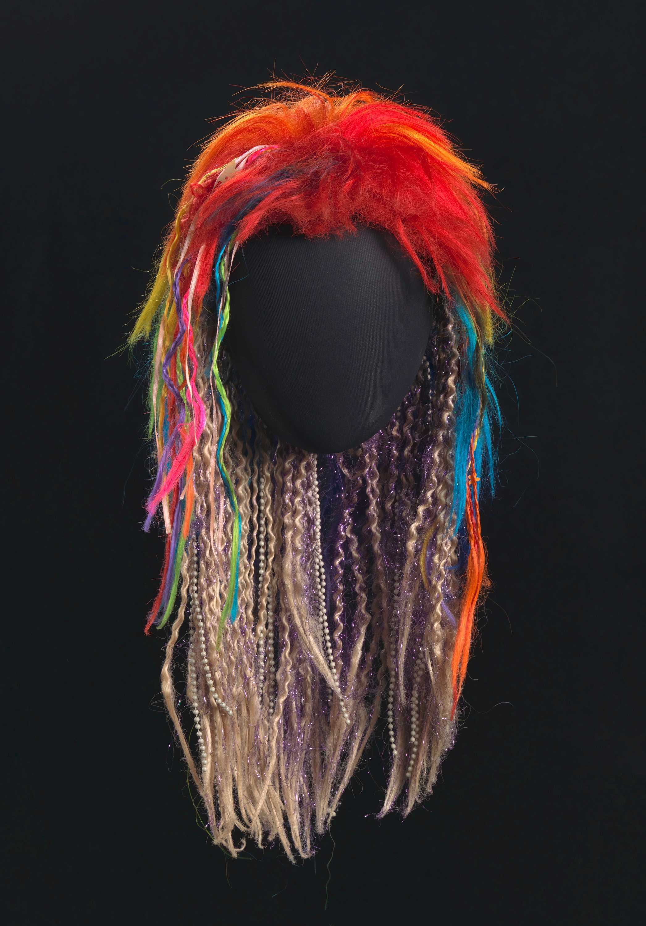 The rainbow wig is in a mullet shape with multiple colors. Some strands are crimped and braided.
