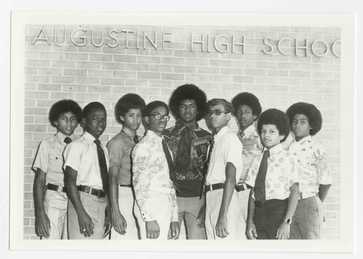 Black and white photograph of Honor Roll student depicts nine young men posing in a group. Standing in front of a brick wall, they stand below large letters that spell "AUGUSTINE HIGH SCHOOL."