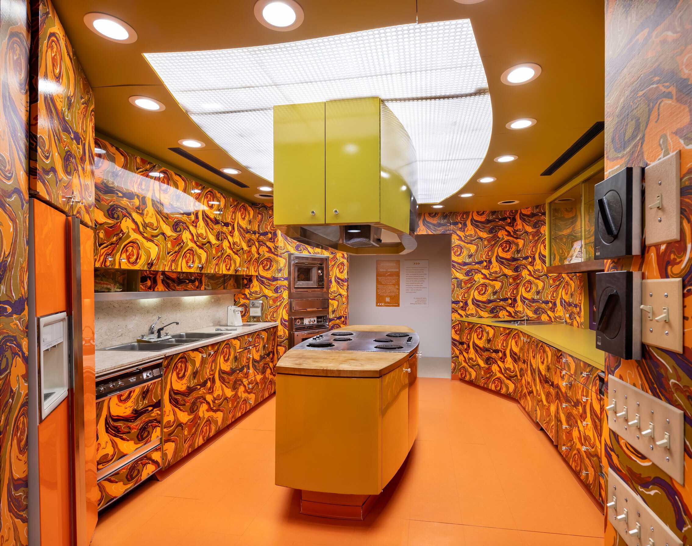 A 70s decor kitchen with a bright orange, purple, and lime green swirl pattern on the cabinets and walls.