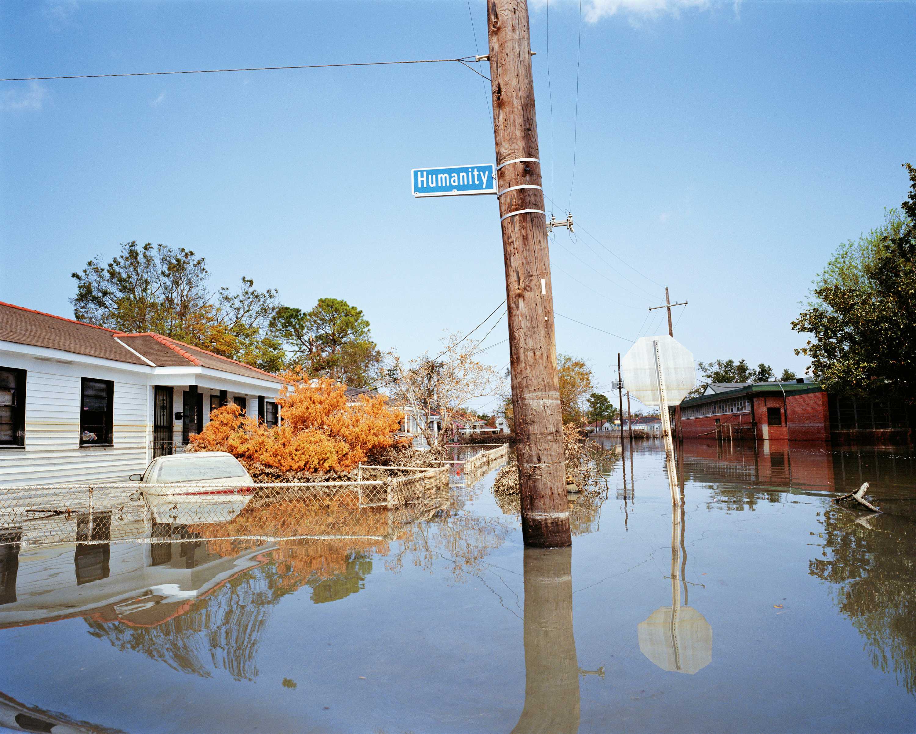 A color image of flooding in New Orleans in the aftermath of Hurricane Katrina. The image depicts a house, car, telephone pole, and stop sign under several feet of standing water along Humanity Street.