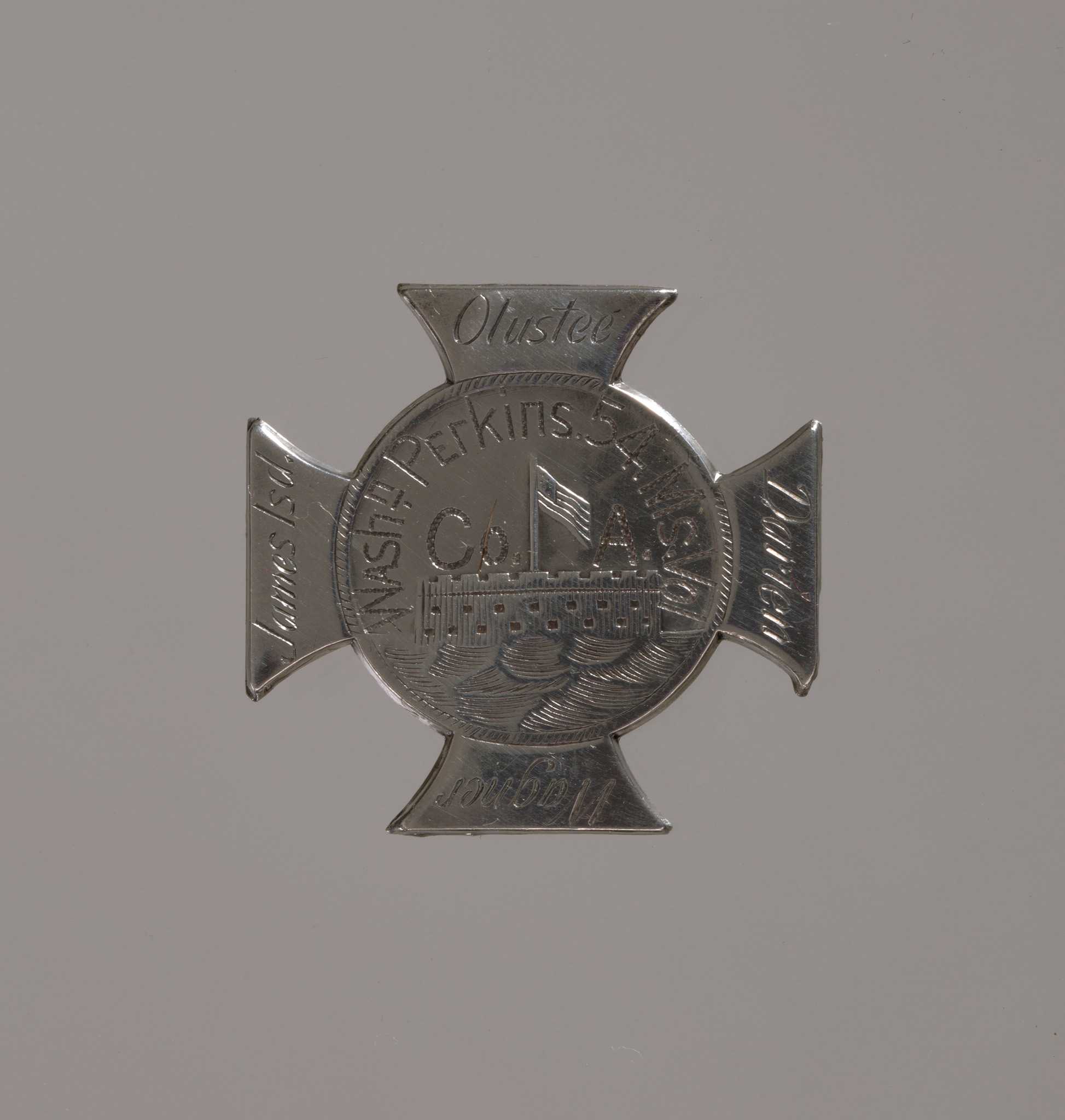 A Maltese cross with a disk at center showing Fort Sumter flying an American flag overhead in raised relief with water in the foreground. The owner’s name [Washnt Perkins 54 Ms. Vol / Co. A] is centered over the fort etched in a half-circle. Each of the arms of the cross is hand engraved with a battle fought by the 54th Massachusetts Infantry — (clockwise from top) Olustee, Darien, Wagner, and James Isd — done in different lettering than the owner’s name. The back of the badge has a T-bar pin closure.