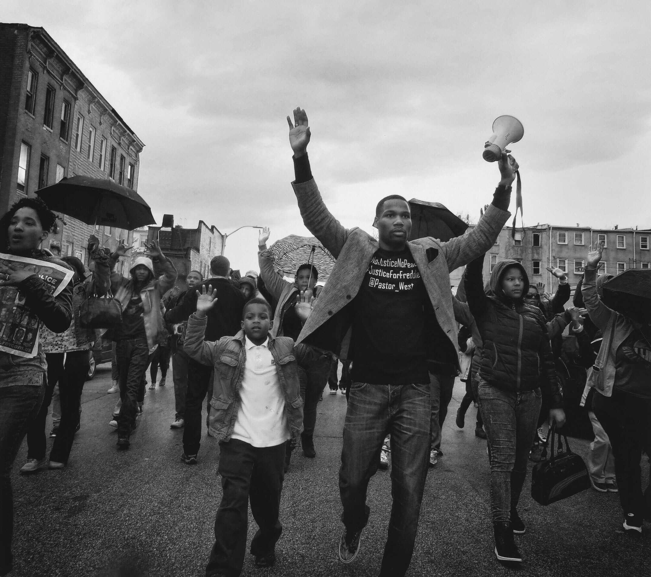 A black and white polaroid picture of a protest. A man and child walk with this hands up in the air.